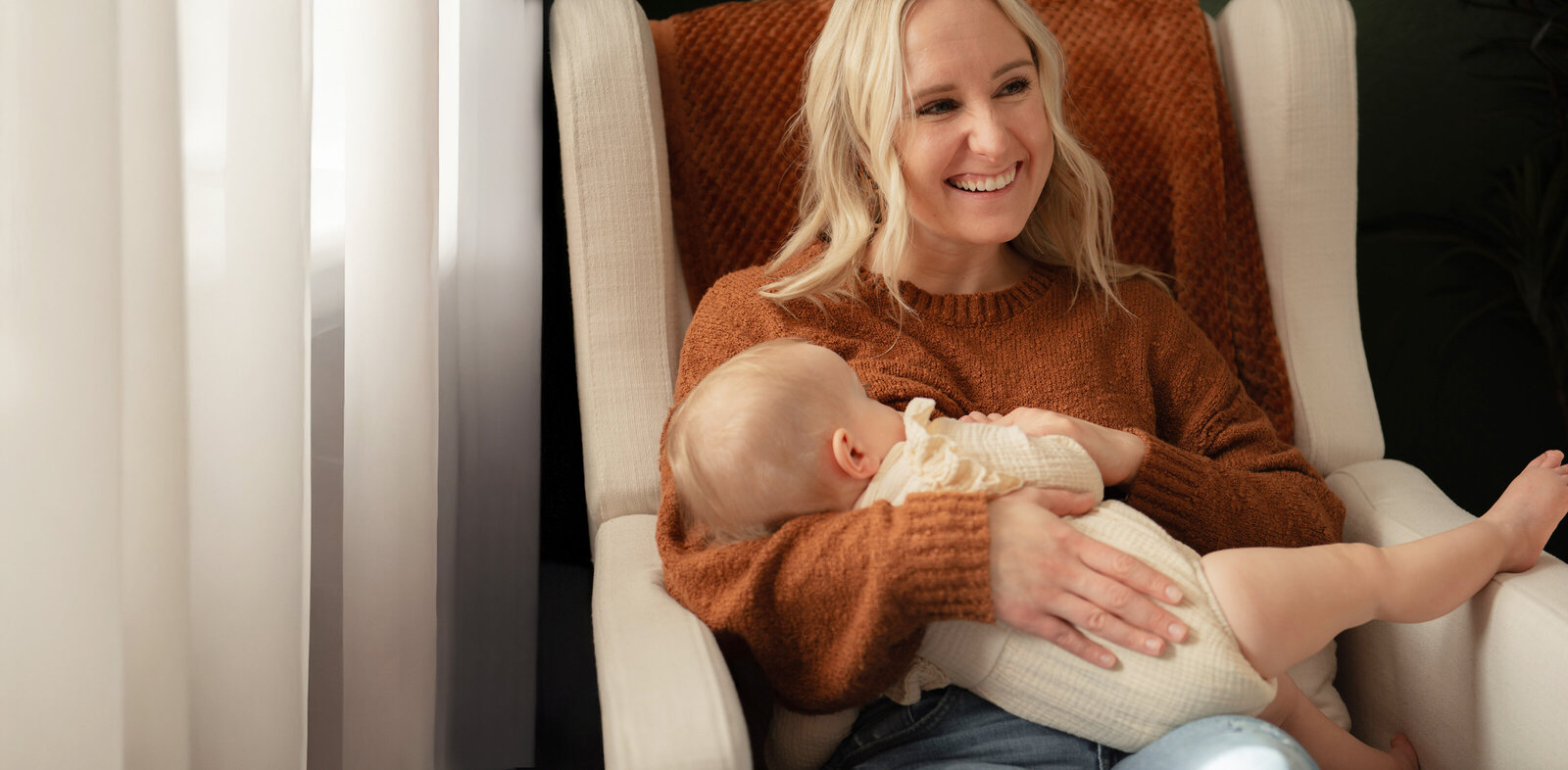 mother smiling in a chair as she breastfeeds baby