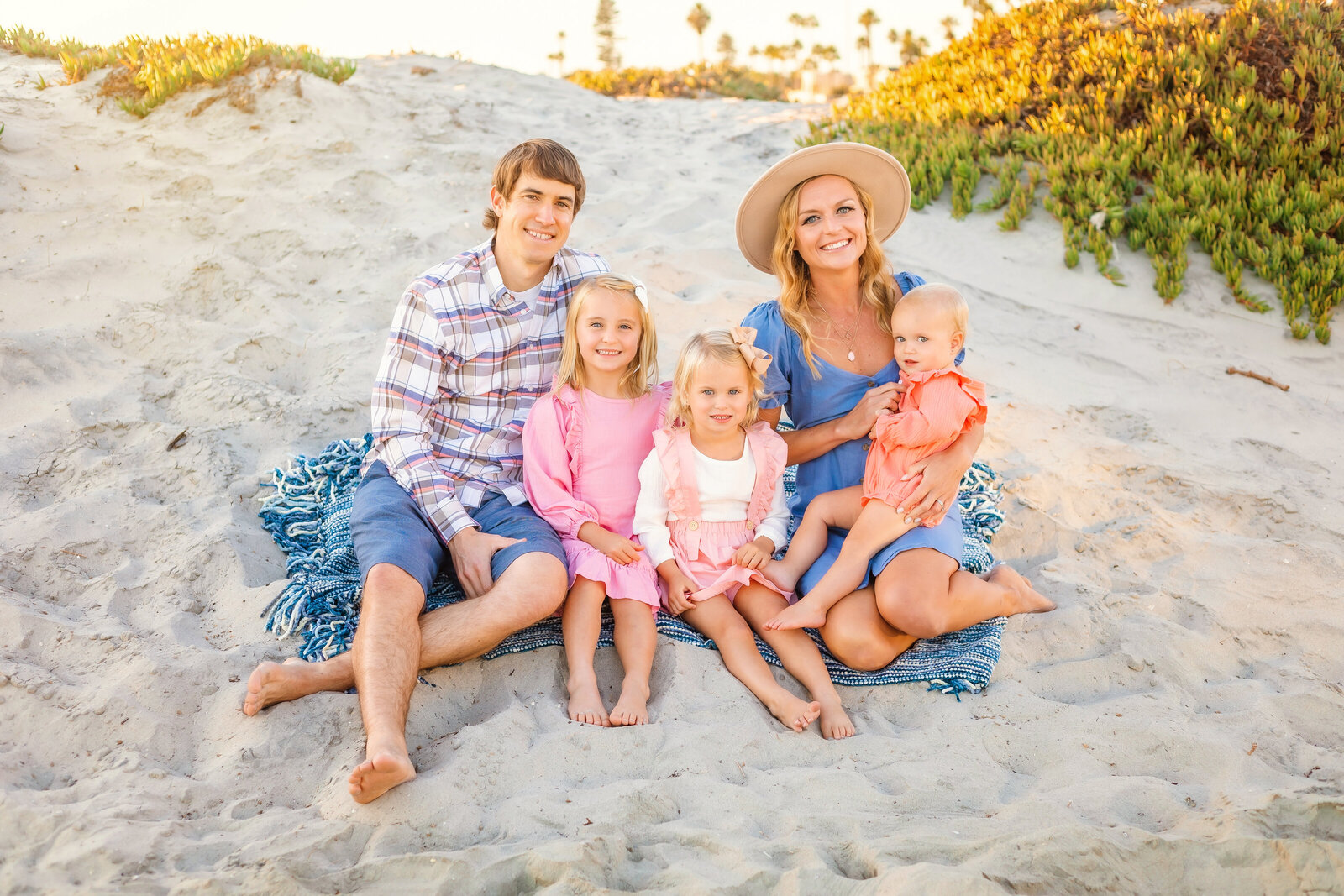 Family Photographer, mom, dad and three kids sit in the sand together