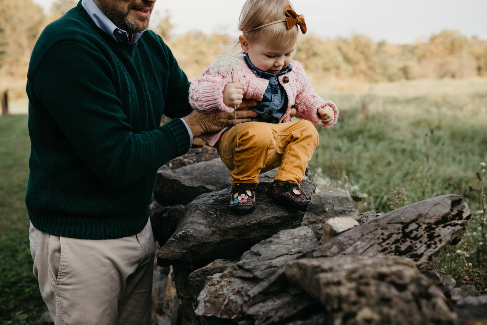 A father helps his little girl walk along a rock wall