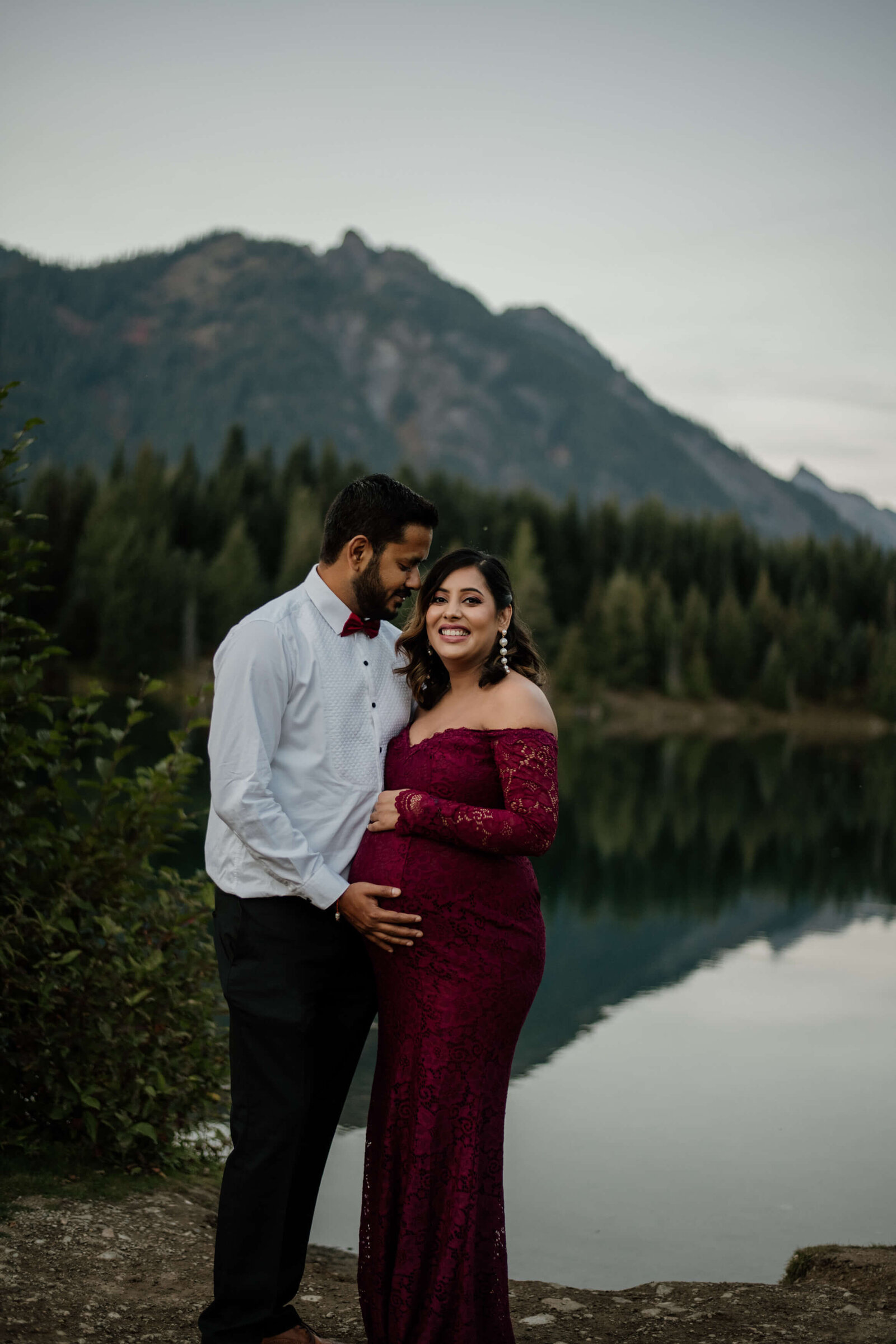 Couple standing together in front of pond and mountain.