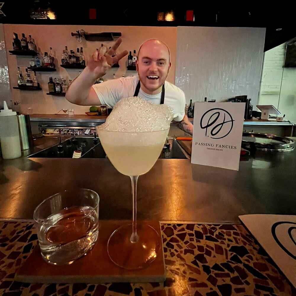 A smiling server in the background, serves a lychee martini