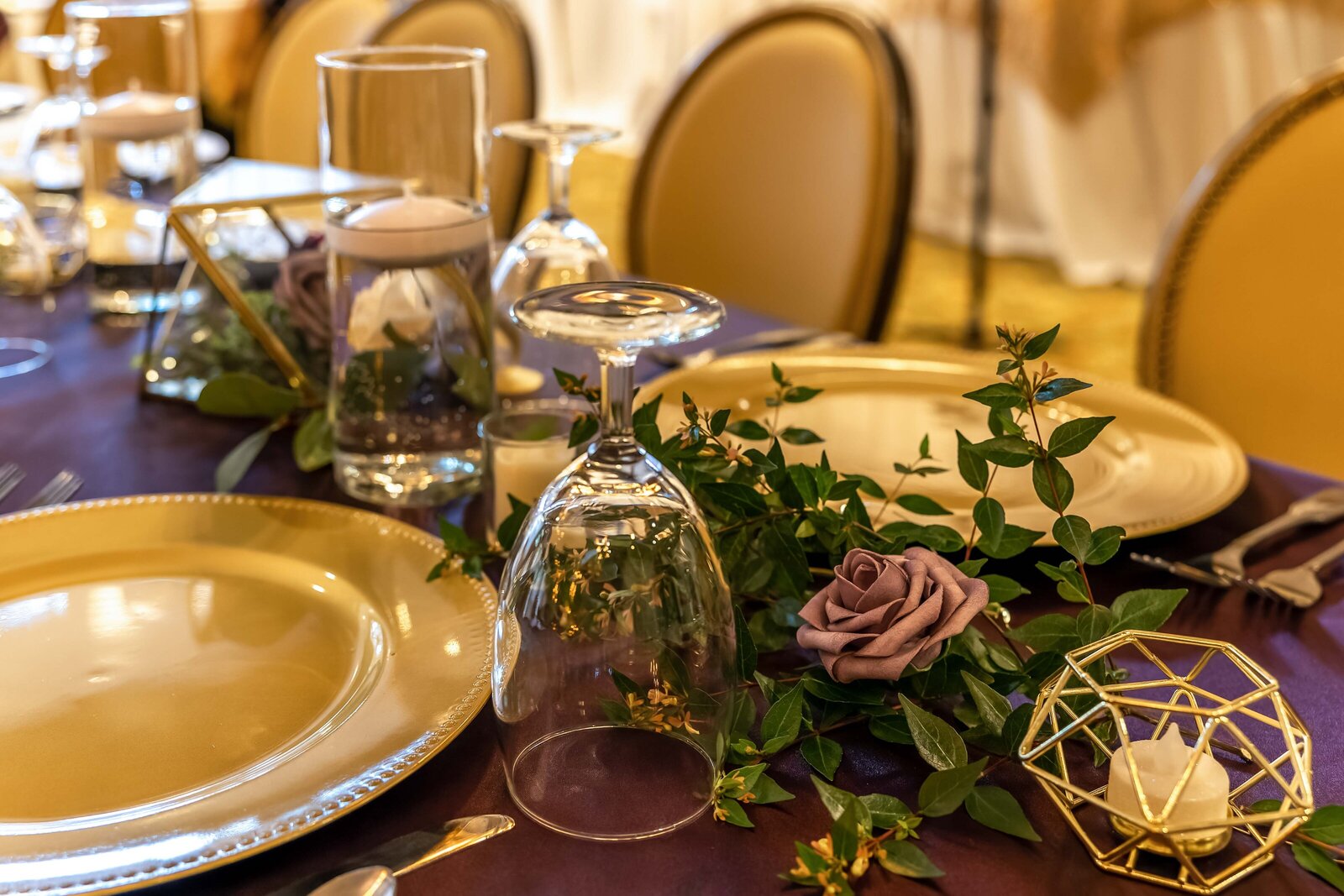 A wedding reception table decorated with gold plates, floating candles in glass vases, and greenery inside a gold frame centerpiece, captured during a Chetola Resort wedding in beatuiful Blowing Rock, NC, showcasing modern elegance.