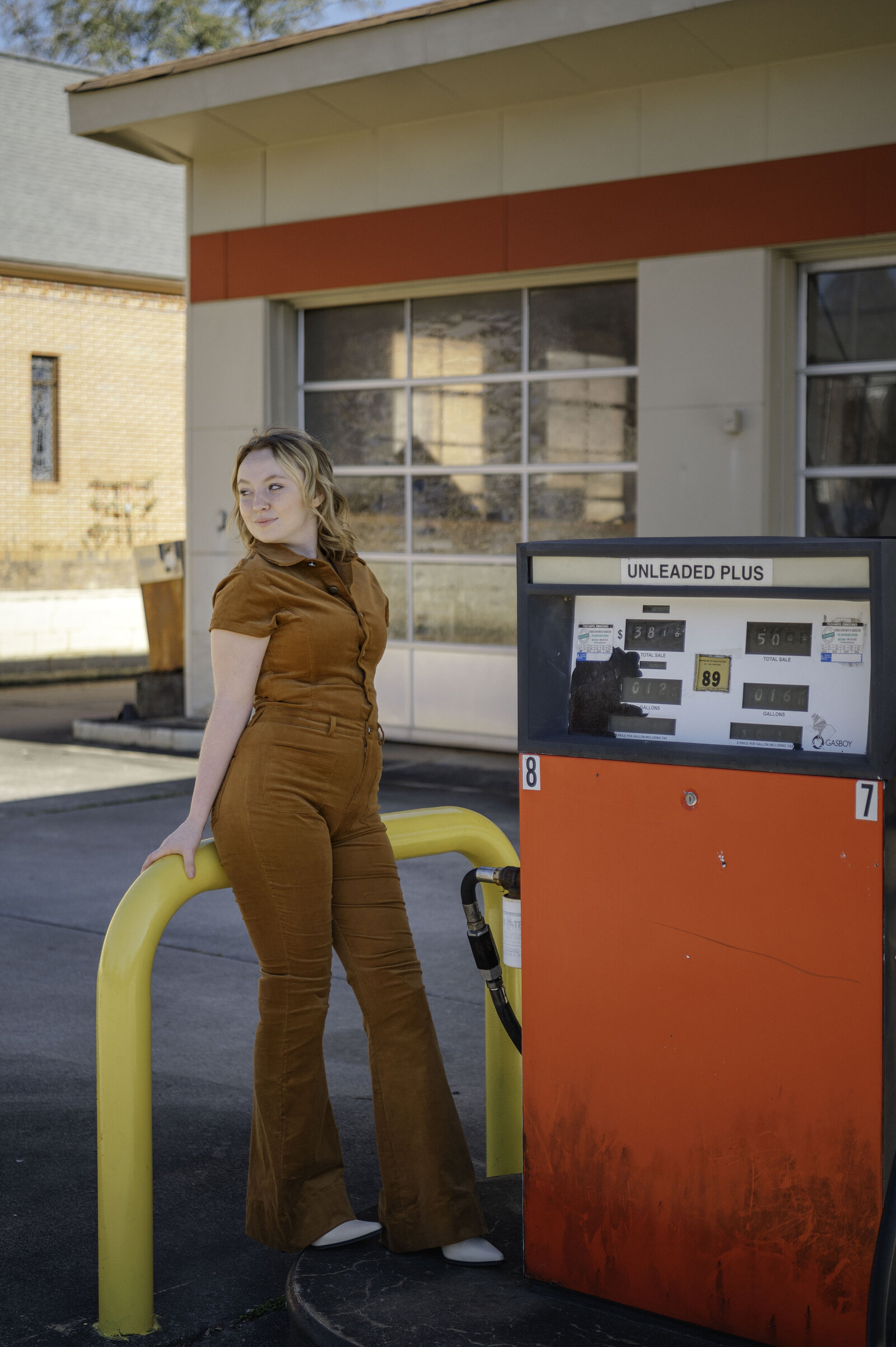 Beautiful senior at gas station wearing a brown jumpsuit with white boots