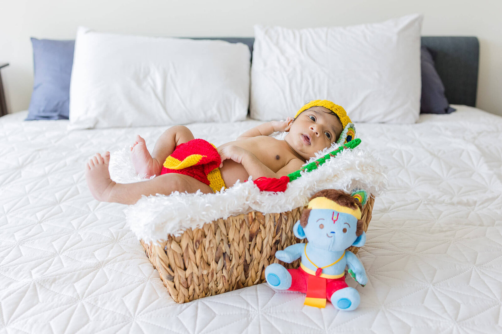 A newborn boy dressed as Krishna and laying in a basket.