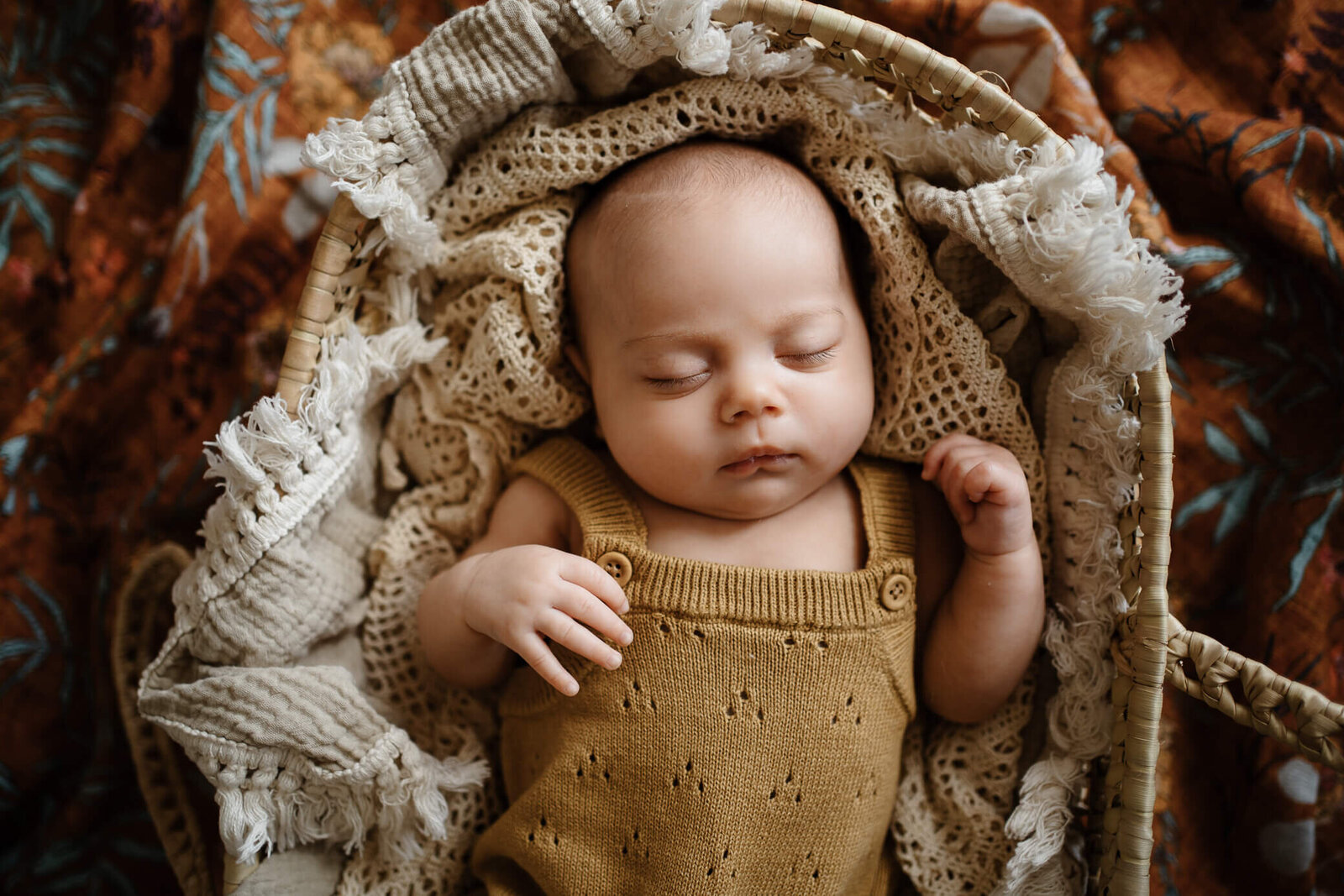 Newborn baby with mustard color knit romper sleeping peacefully