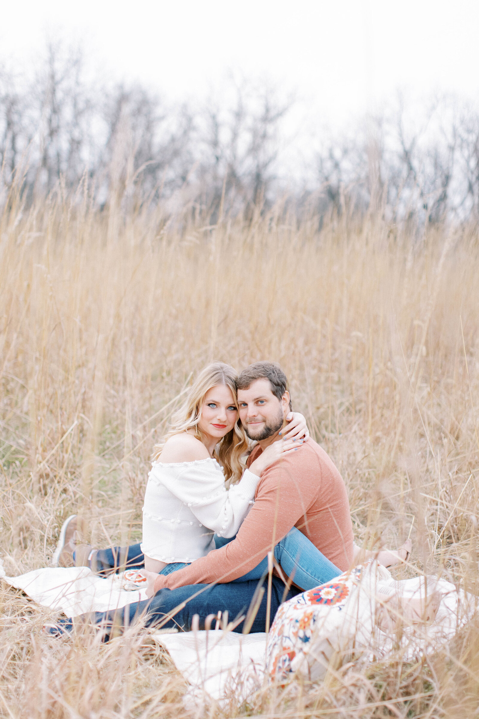 Couple snuggle in close at picnic champagne engagement session at James A Reed in Lees Summit