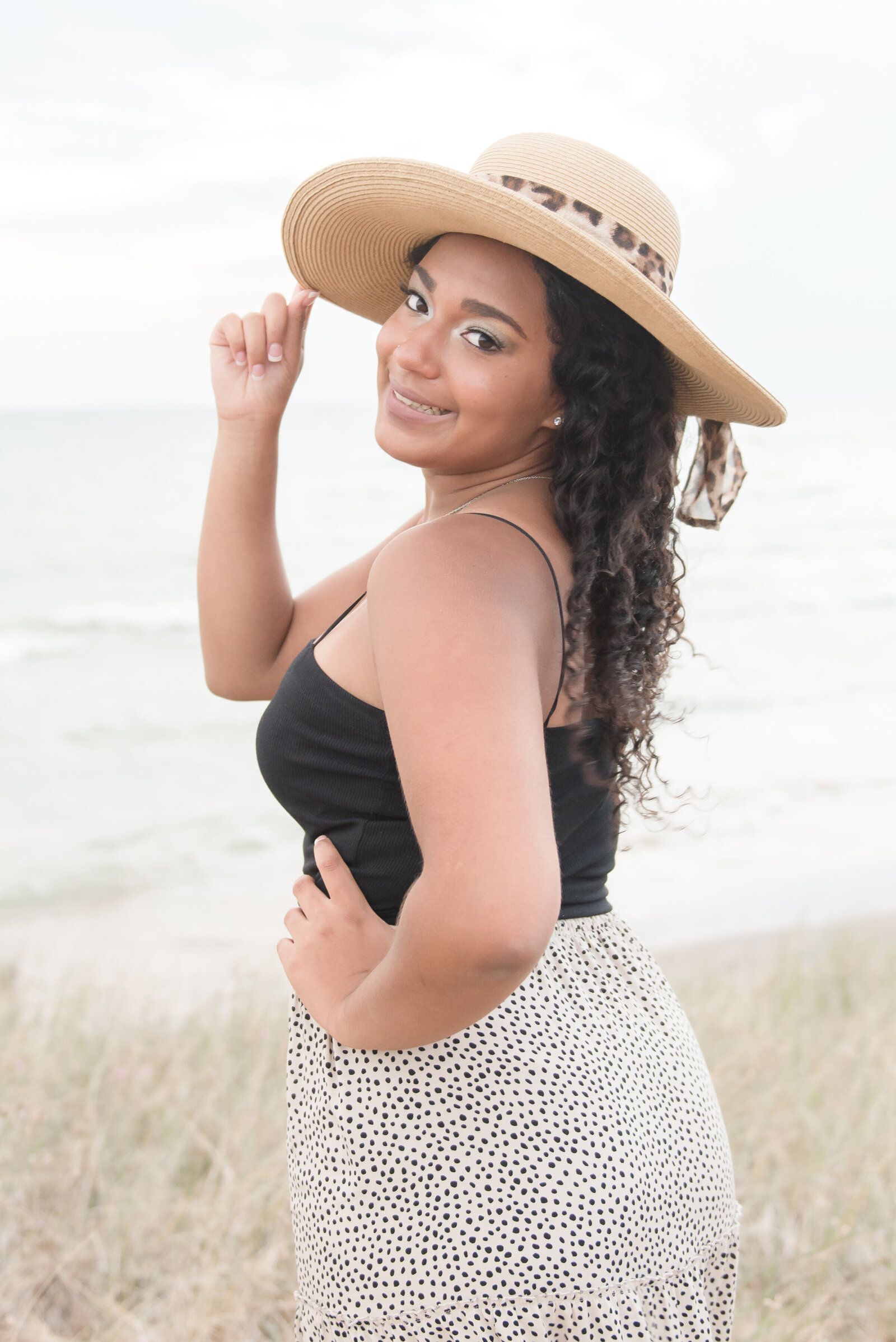 senior girl standing looking back over shoulder with one hand on her hat in Ludington