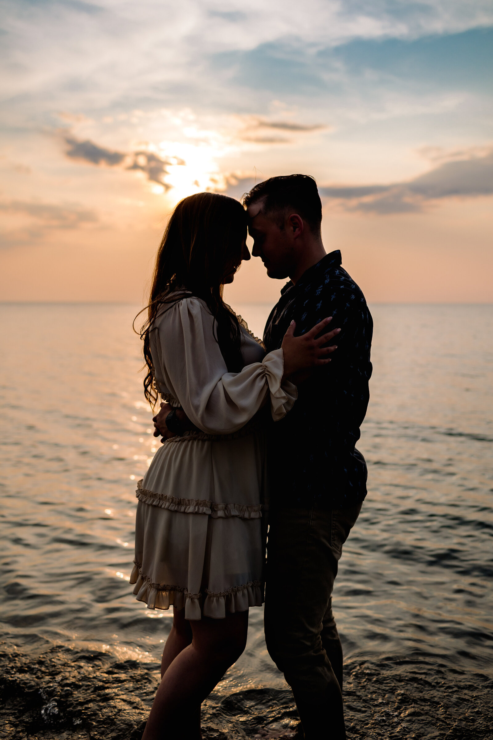 Couple stands forheads together against a beautiful lake Erie sunset