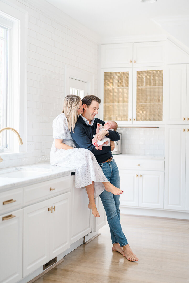 Couple cuddles together in kitchen while dad holds baby