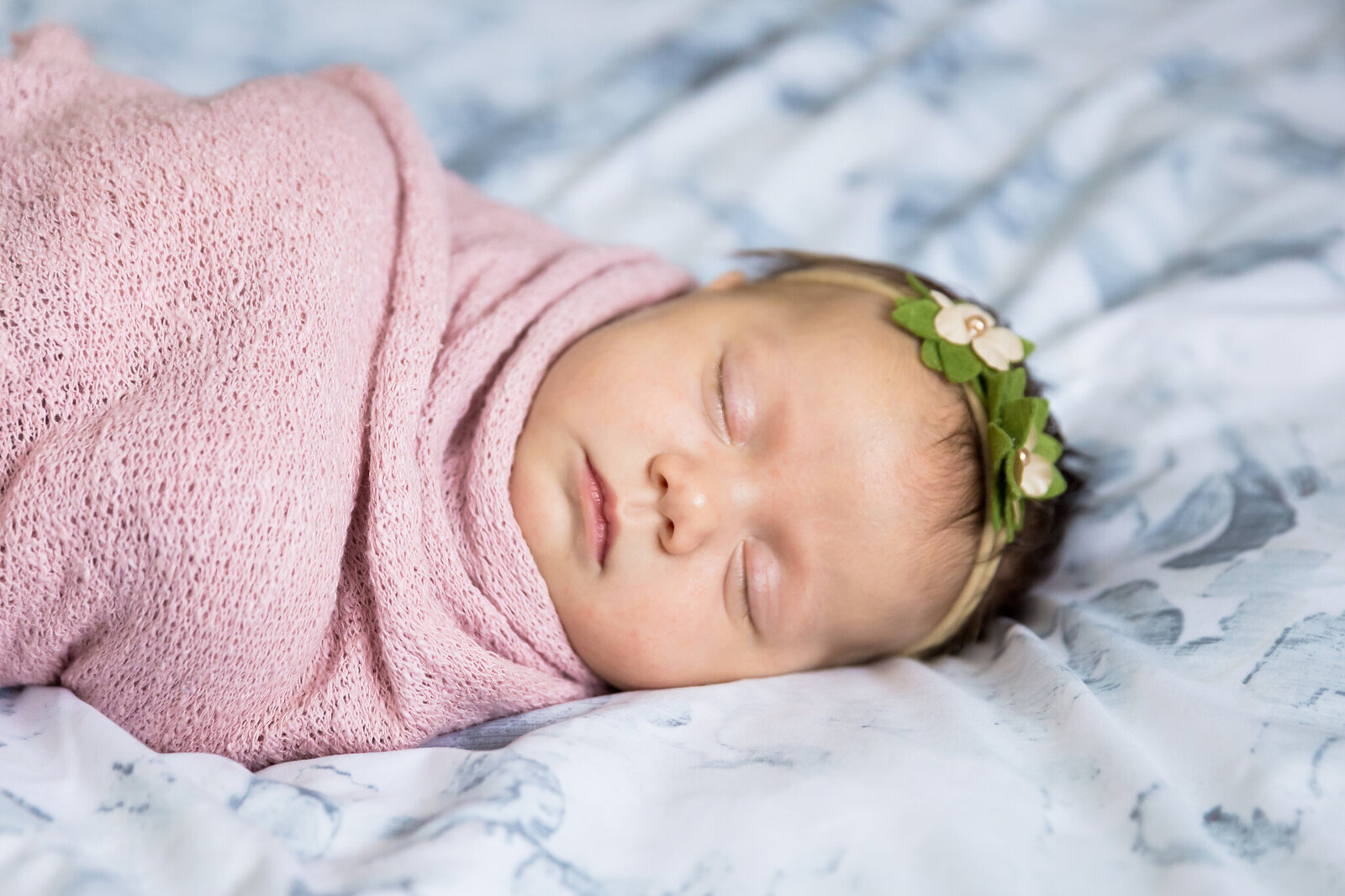 Newborn girl wrapped in pink blanket on a bed