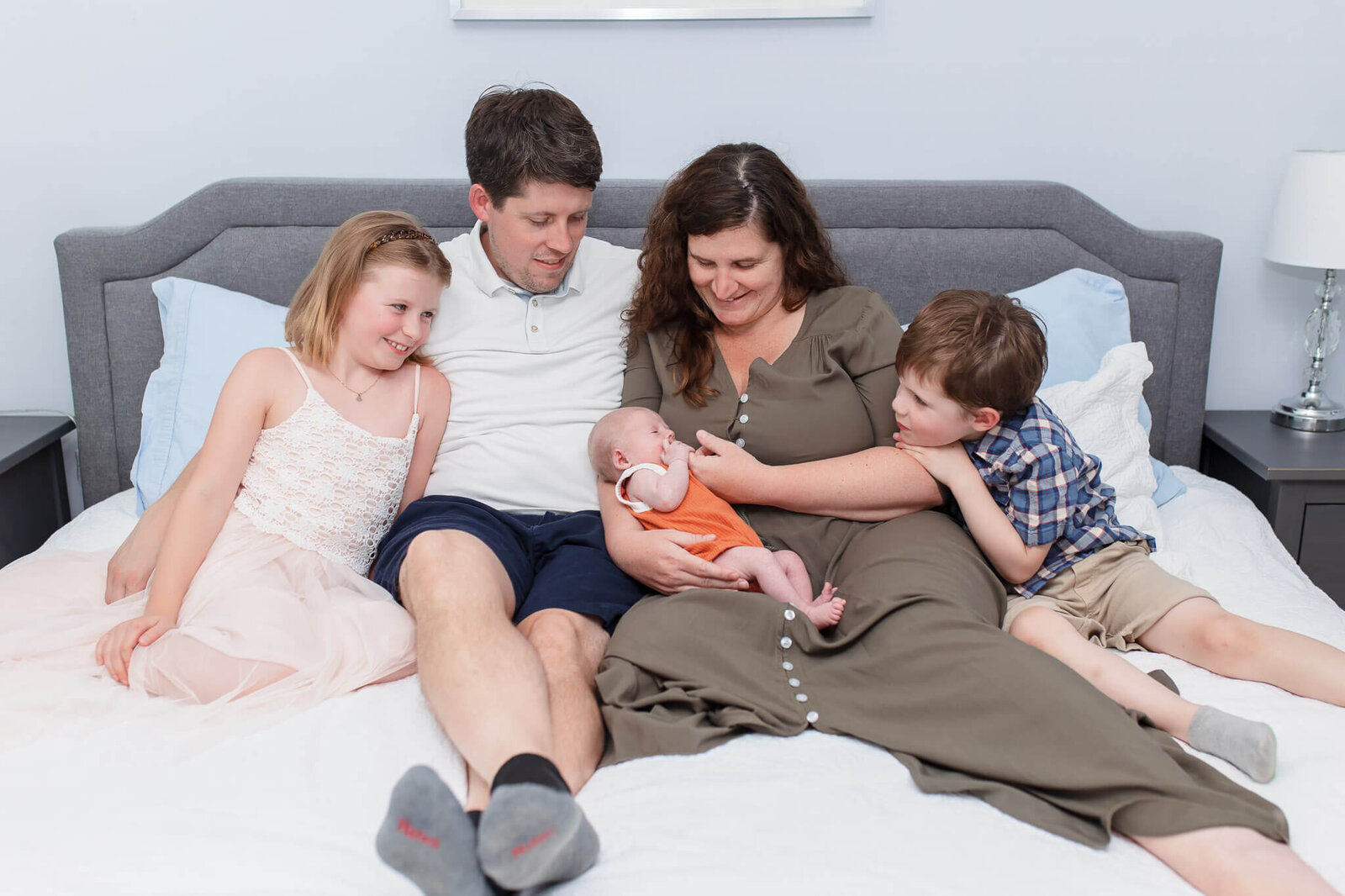A mom and dad with their three children snuggling in bed.
