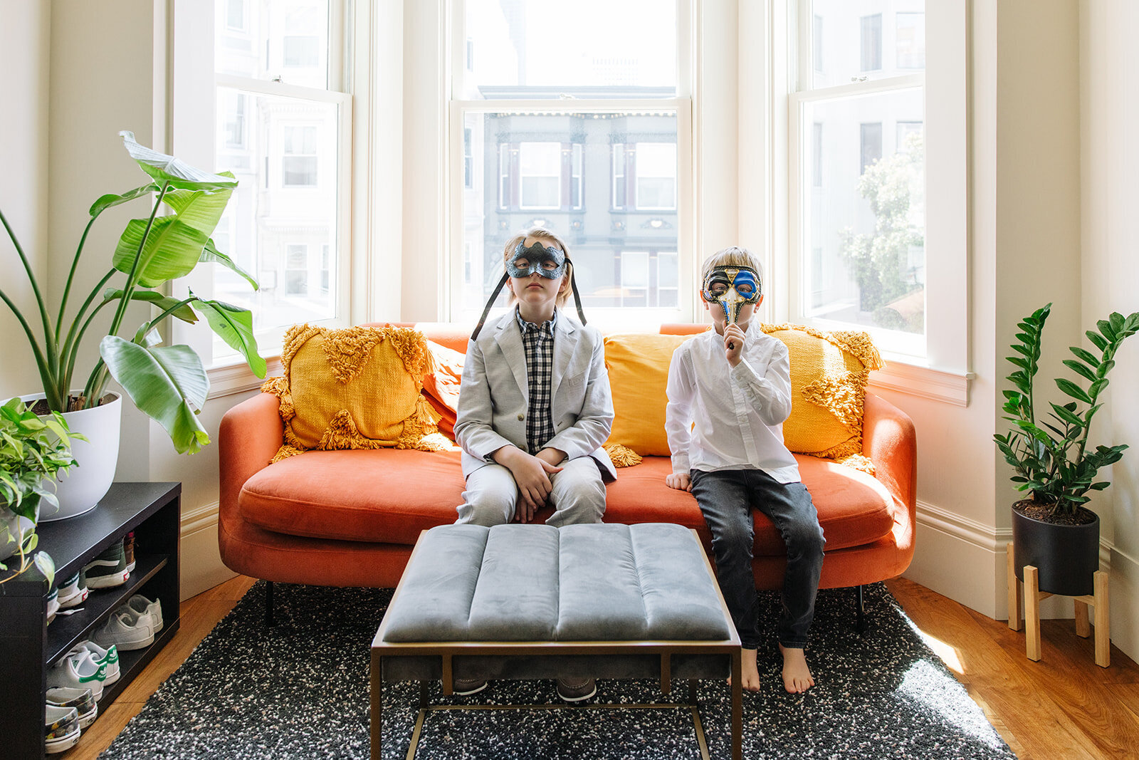 two boys wearing dress clothes sitting on orange couch and wearing masquerade masks