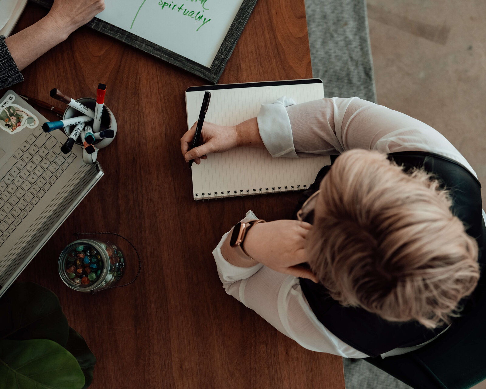And over head perspective of two women during a meeting as they collaborate, wearing office attire, sitting at a beautiful wooden table with succulents.