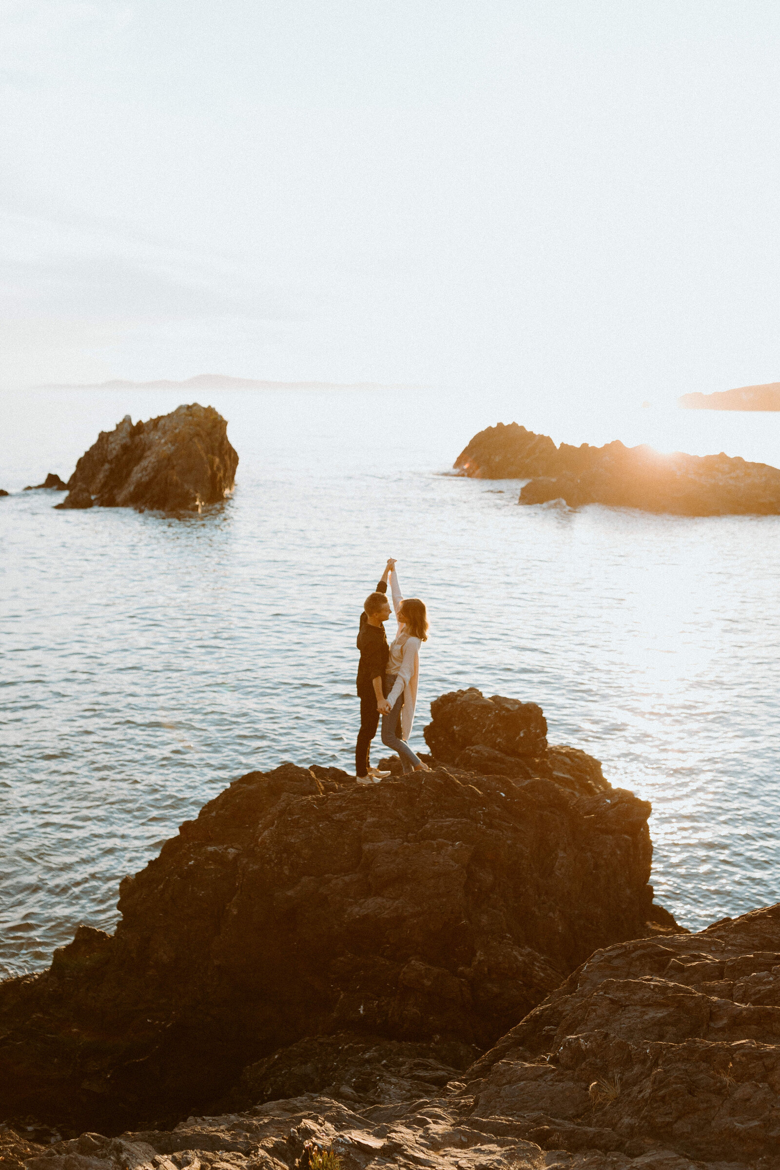 couple holding eachother on a rock by the ocean