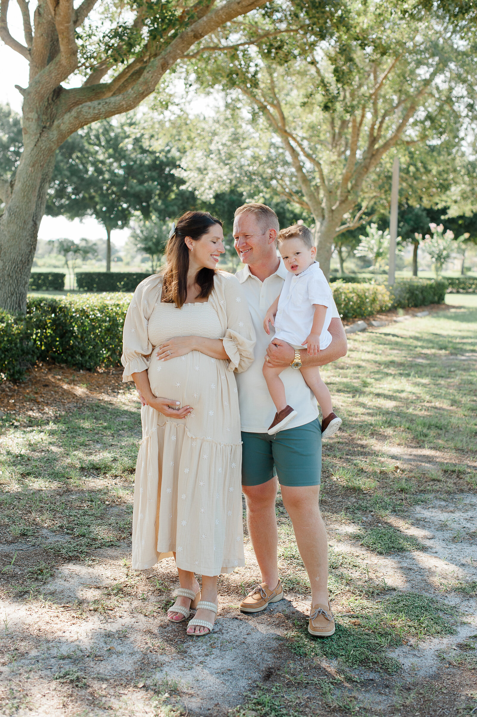 Pregnant couple smiling at each other while dad holds their son