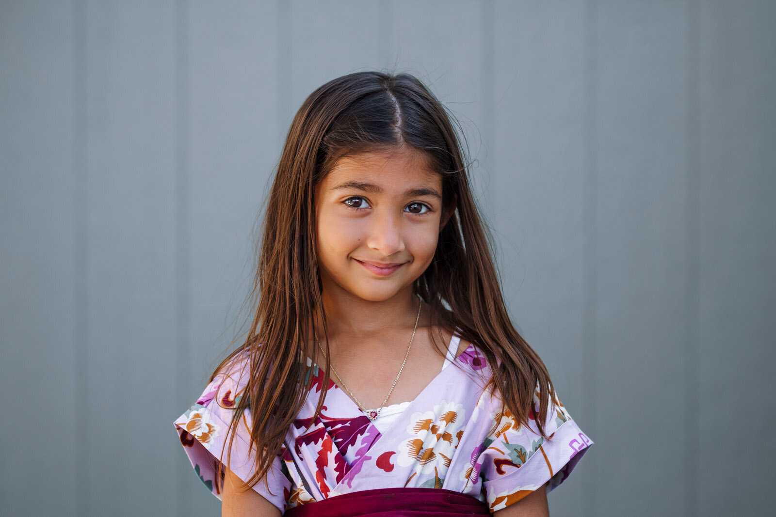 school photo of a girl smiling at the camera while standing in front of a slate blue wall at her Oakland preschool