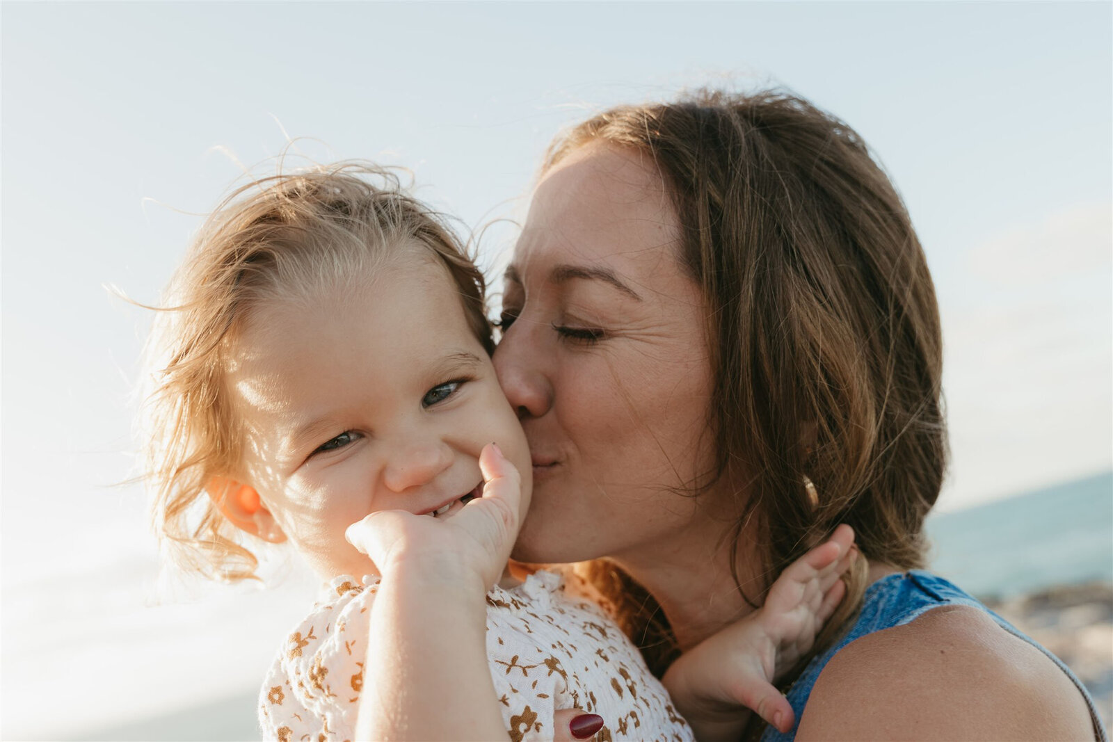 Mother and daughter embracing during a Maui cliffside family photo shoot, natural light highlighting denim and soft neutrals.