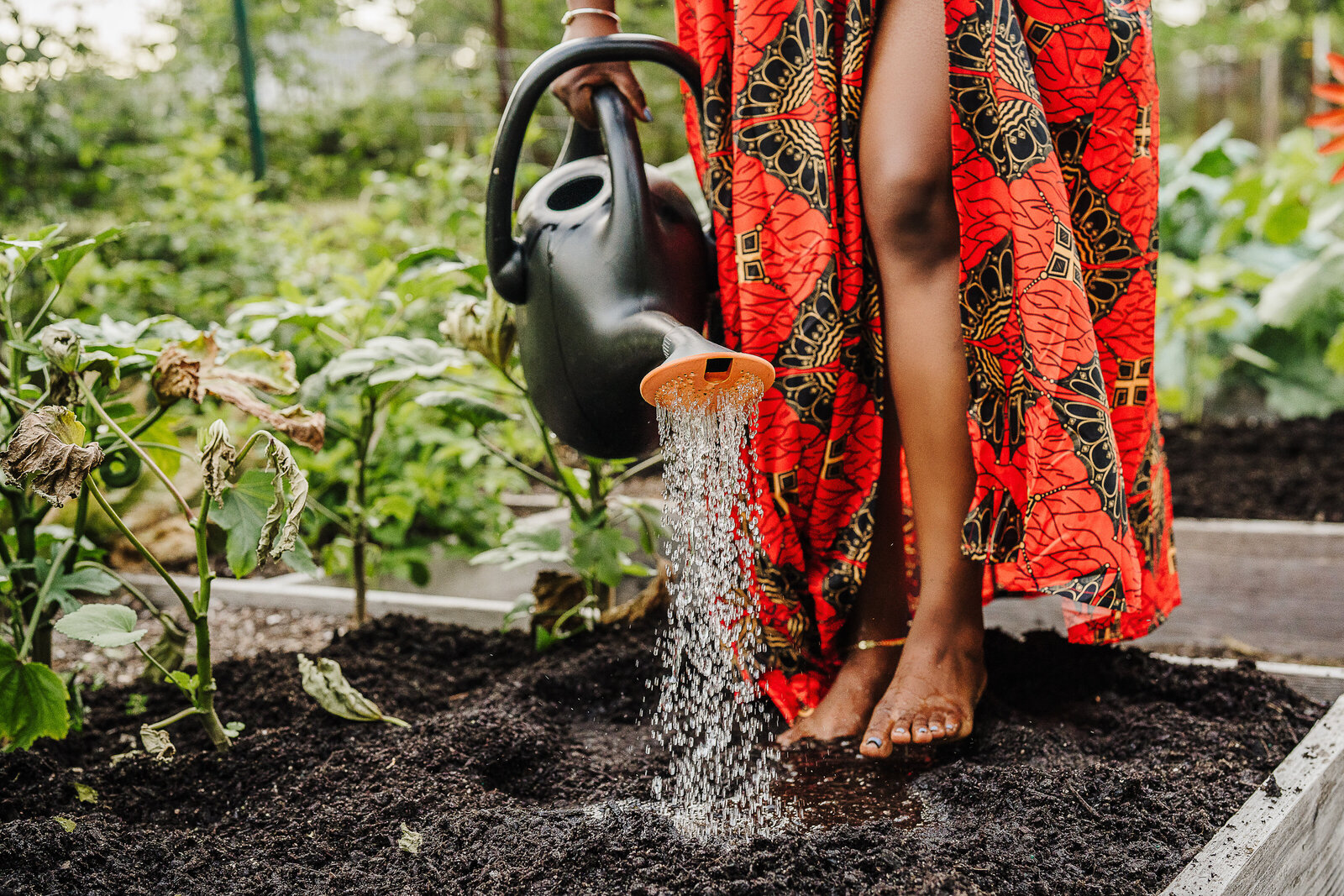 woman in African dress in garden barefoot pours water