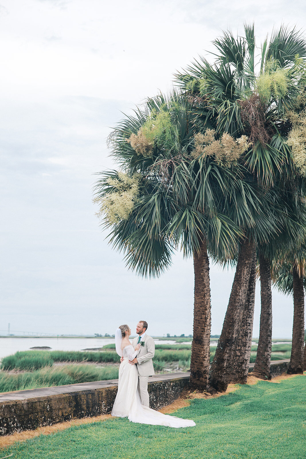 Bride and Groom look at each other in front of palm trees and overlooking marsh at Jekyll Island Club Resort wedding