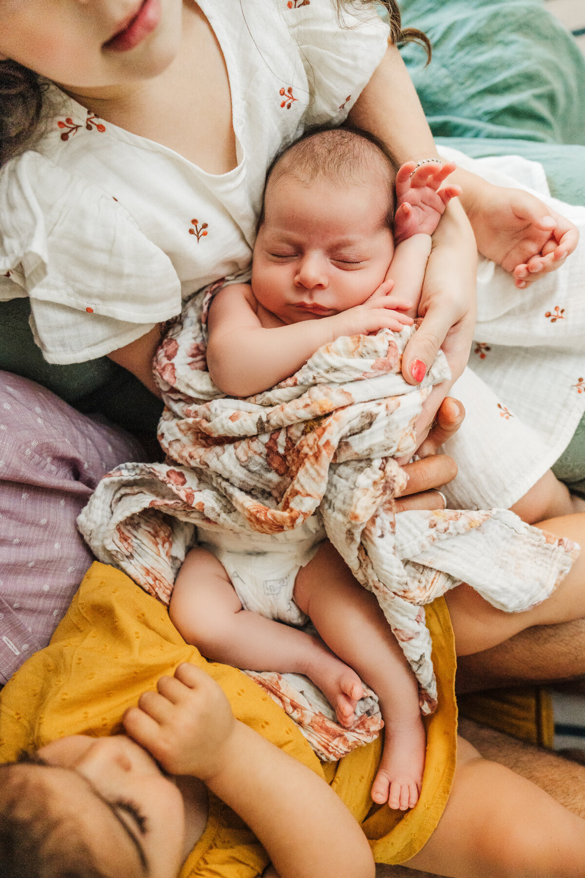 overhead shot of an infant girl wrapped in a floral wrap laying on sisters laps