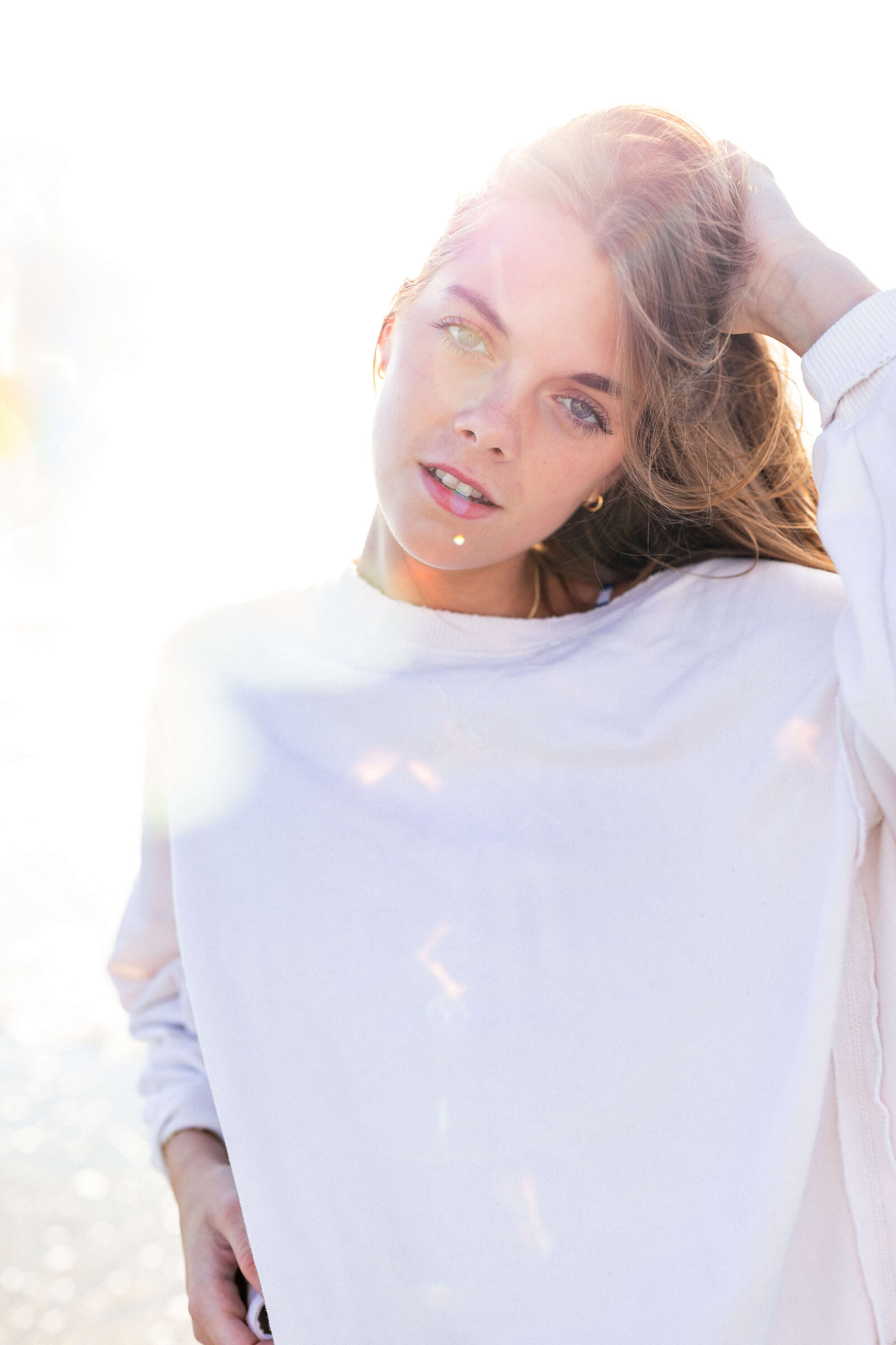 brunette high schooler posing on a beach wearing a white shirt