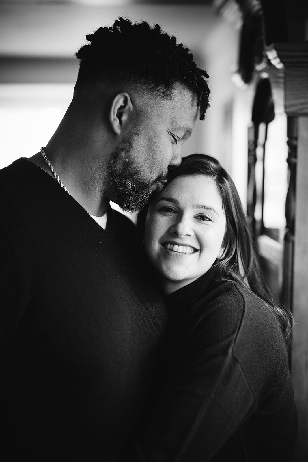 Heartfelt black-and-white photo of a couple embracing, with the man kissing the woman on the forehead.