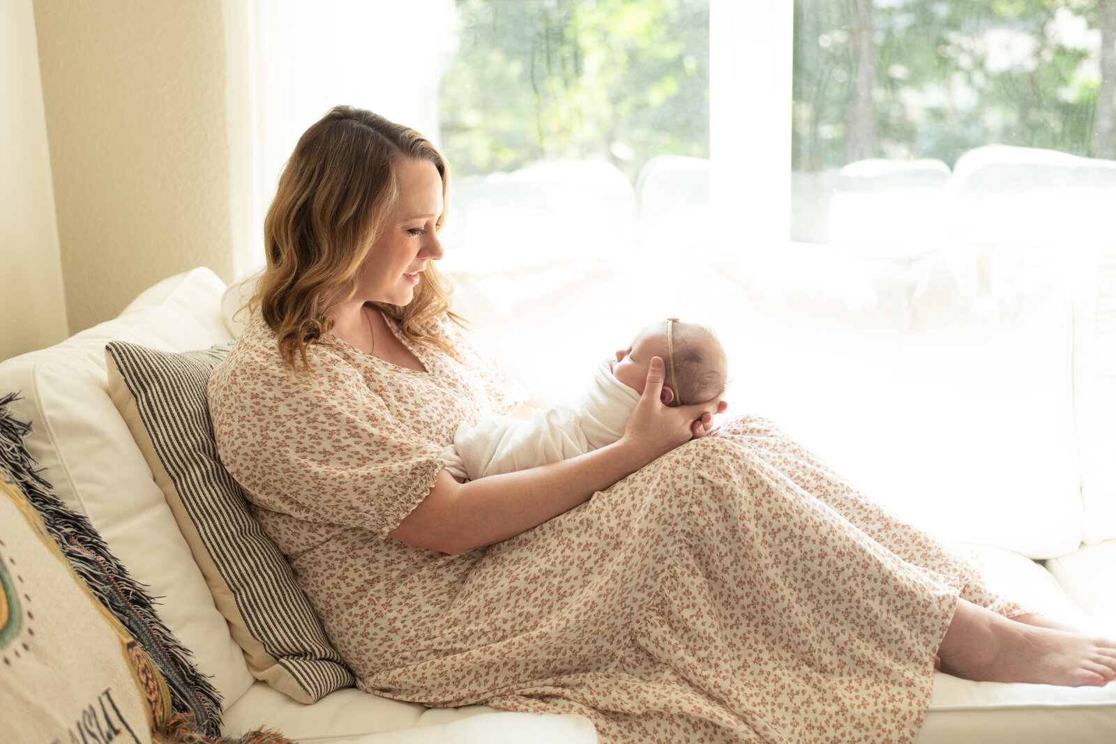 Mother rocks her newborn in soft window light, capturing the quiet beauty of motherhood. A lifestyle newborn session by Moments in Light Photography.