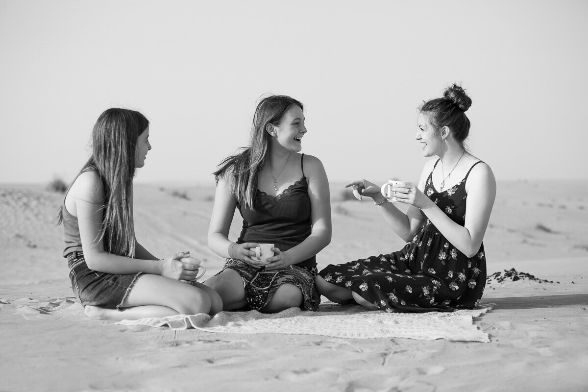 Black and white photo of three young sisters chatting in desert dunes by Vancouver family photographer Yuliia Terziian Photography