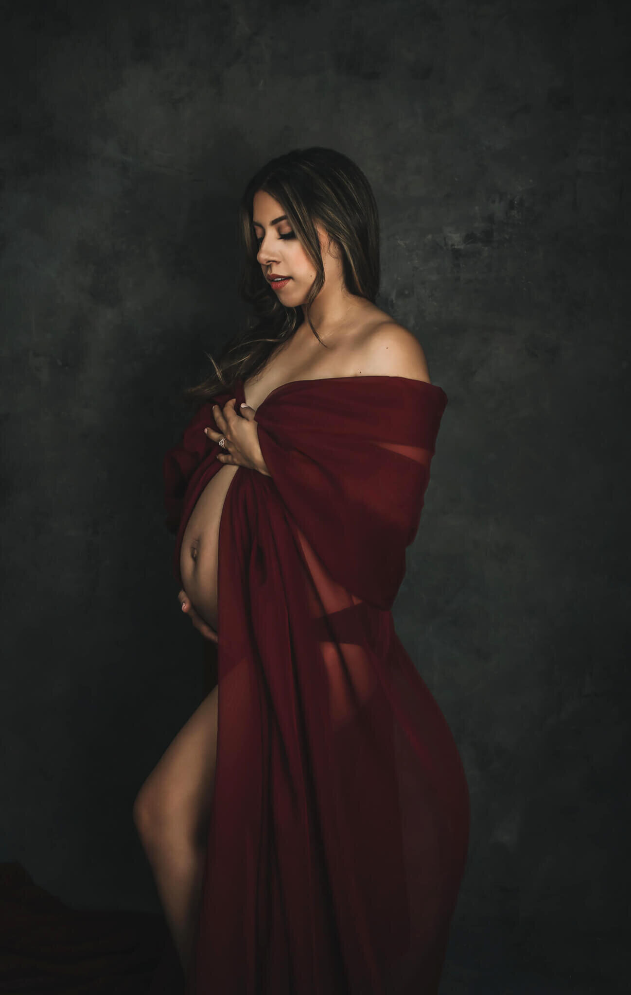 Portrait in color of a maternity photoshoot where the mom to be is wearing a red dress