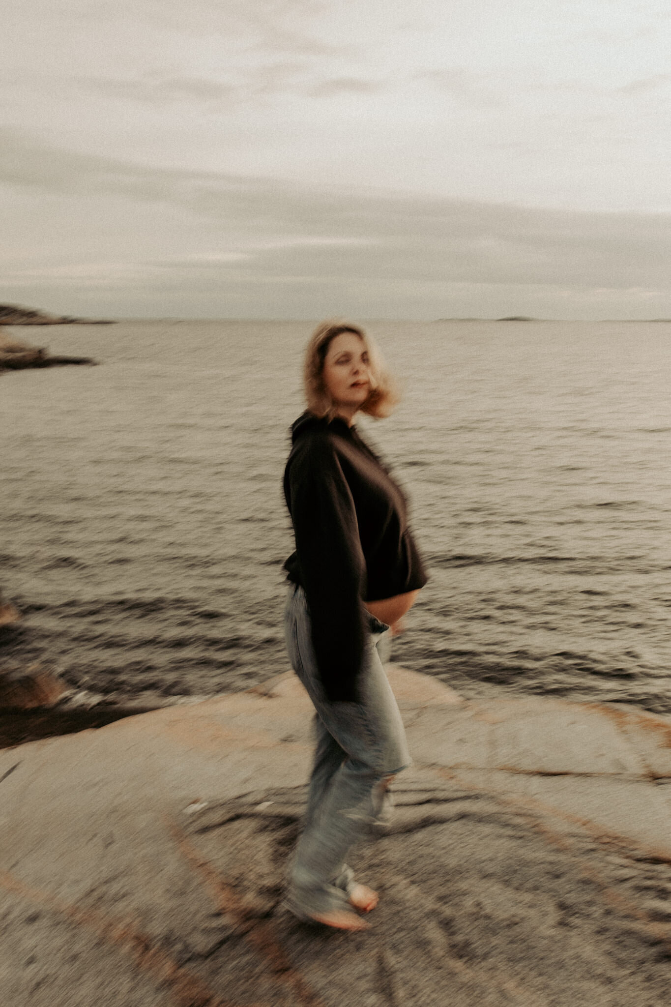 en gravid kvinna står vid havet iklädd  trasiga jeans och tröja