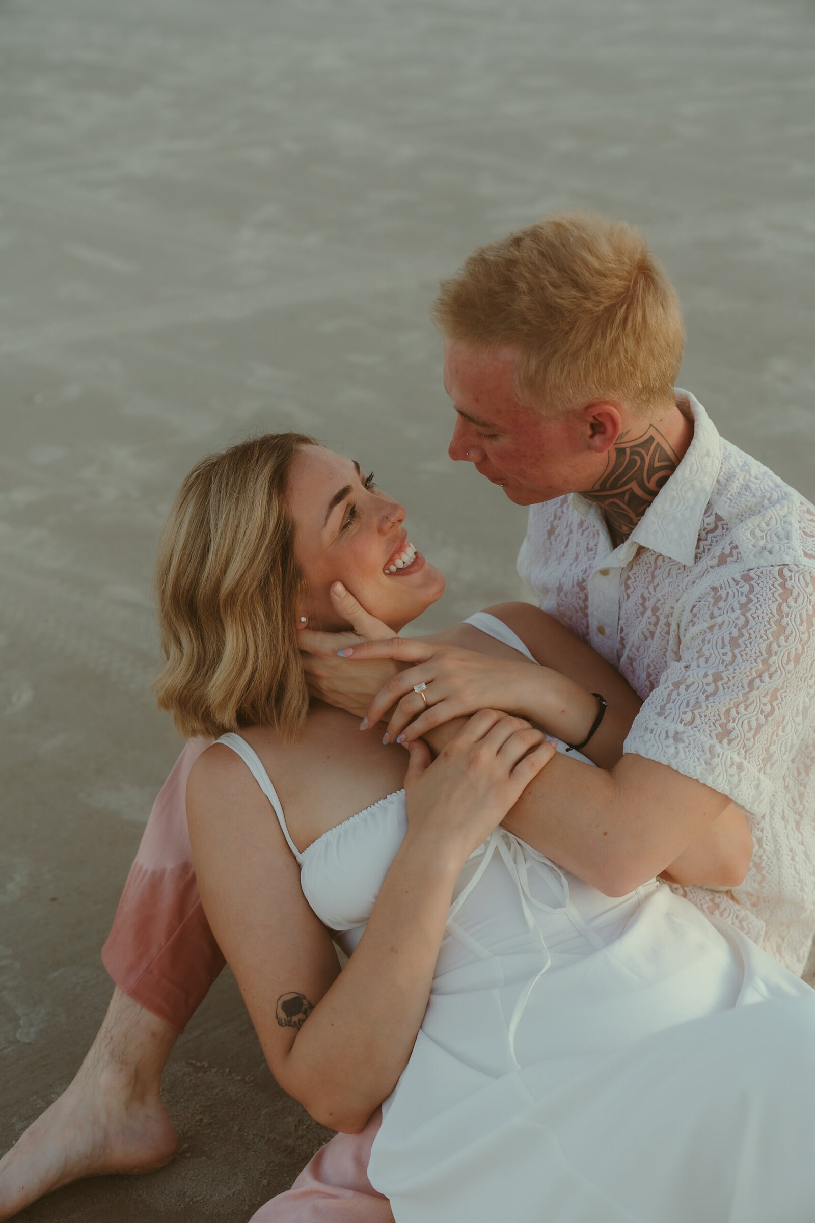 Playful beach engagement session with a joyful couple cuddling in the sand during golden hour in Cocoa Beach.