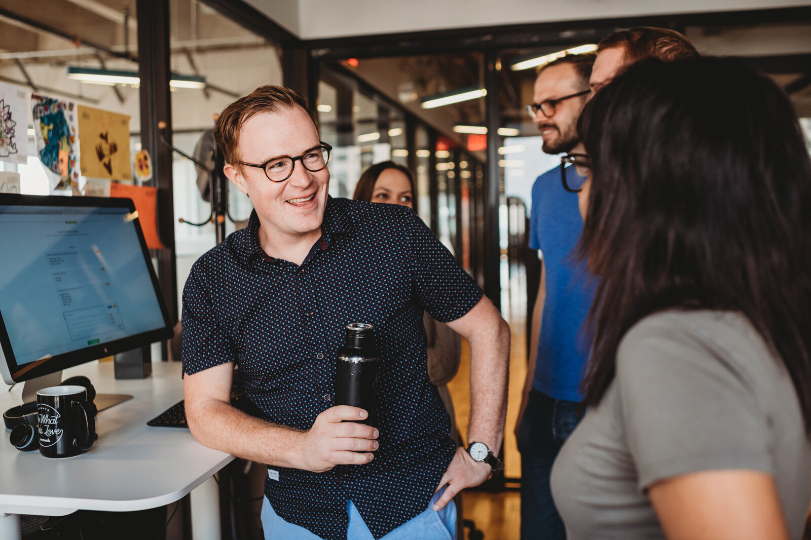 Branding Photographer, a man leans on a standing desk and holds a drink while talking to people at a mixer