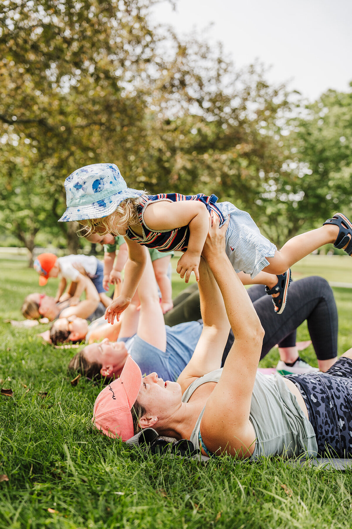 mommy baby yoga class holding kids in air outdoors on exercise mats