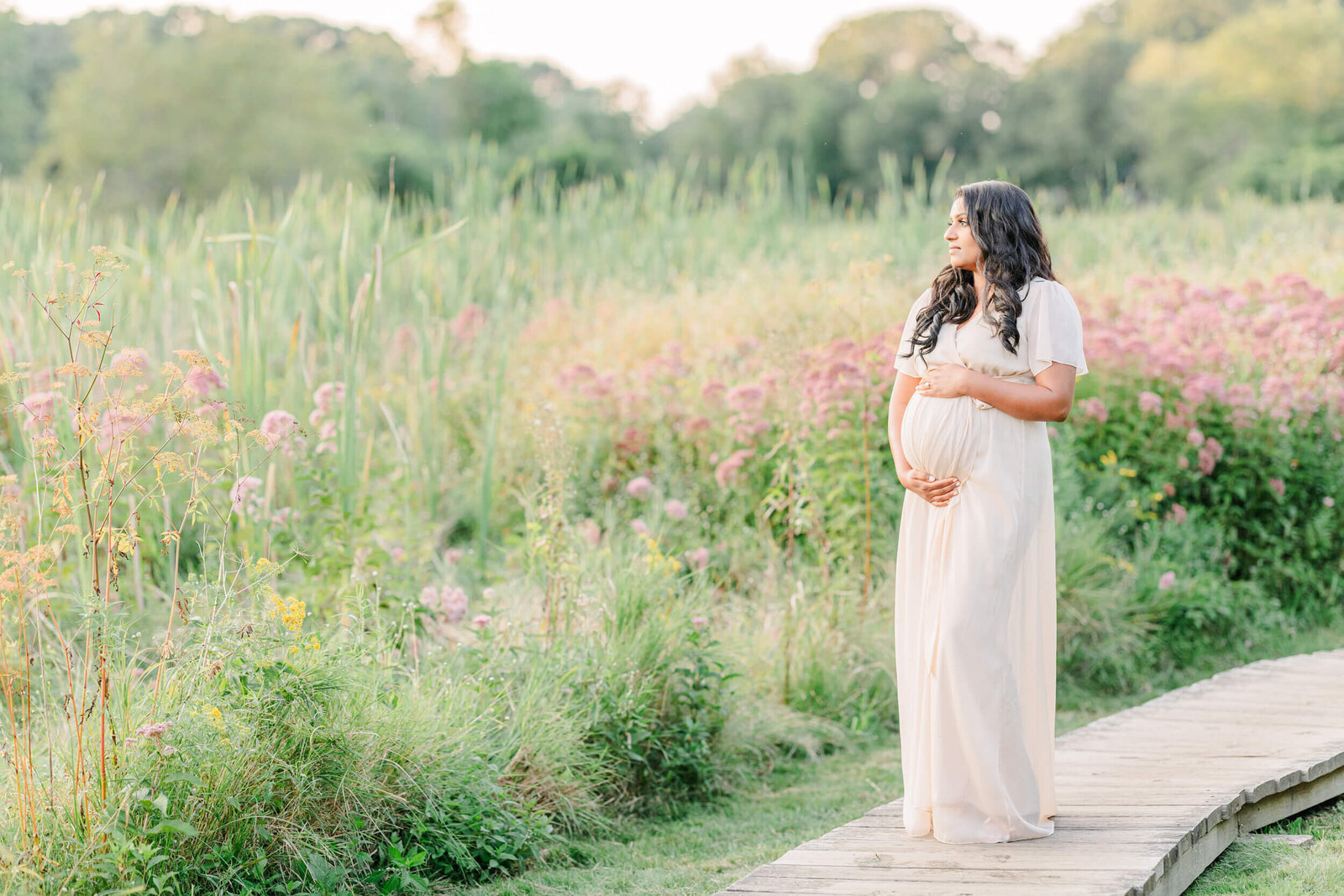 Pregnant woman cradles her baby bump in a field of wild flowers and looks into the distance