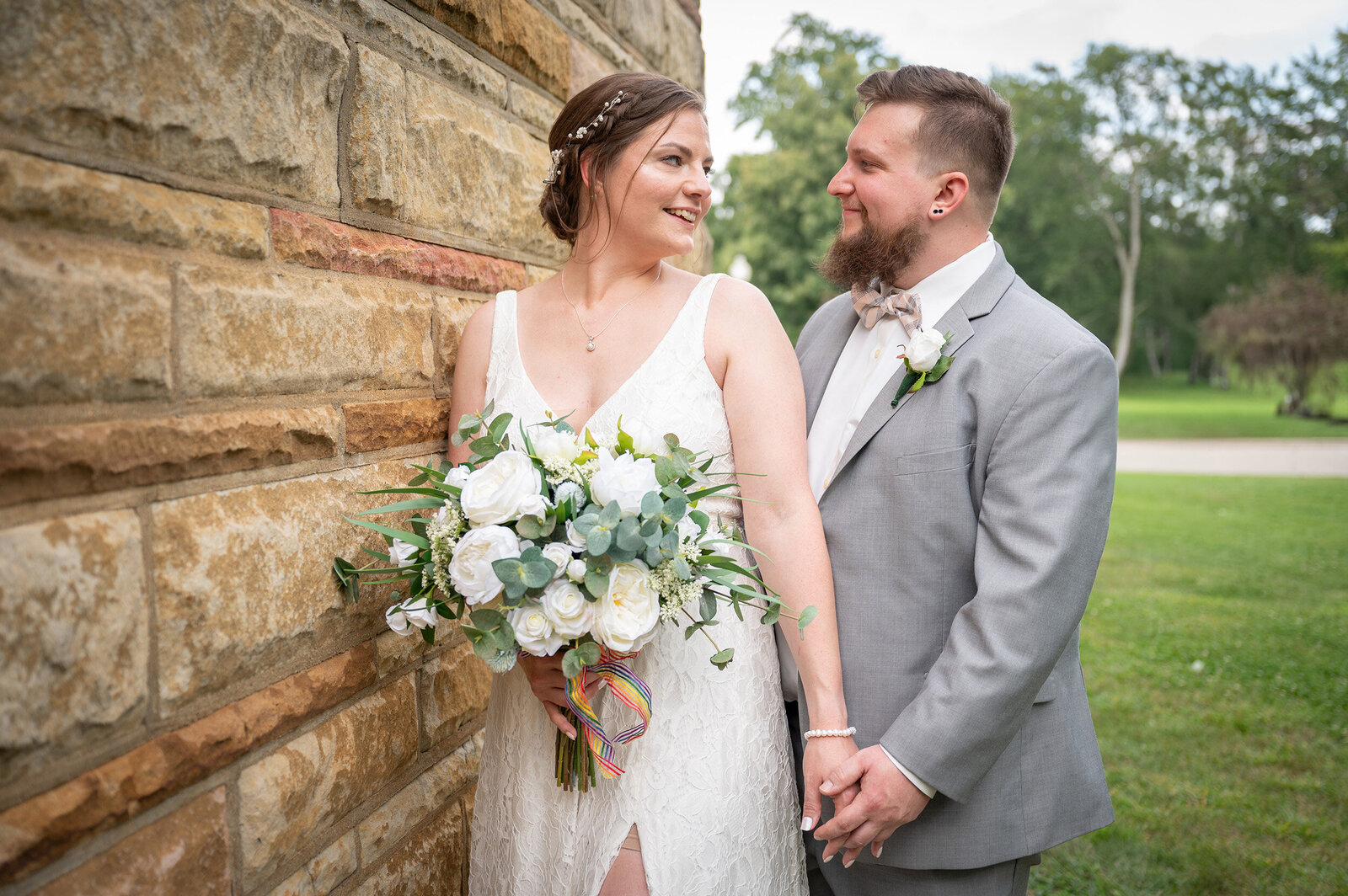 bride and groom look toward one another beside a brick wall