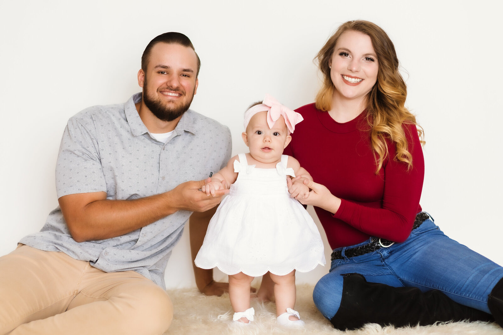 Milestone Photographer, a mother and father hold their baby girl as she stands between them