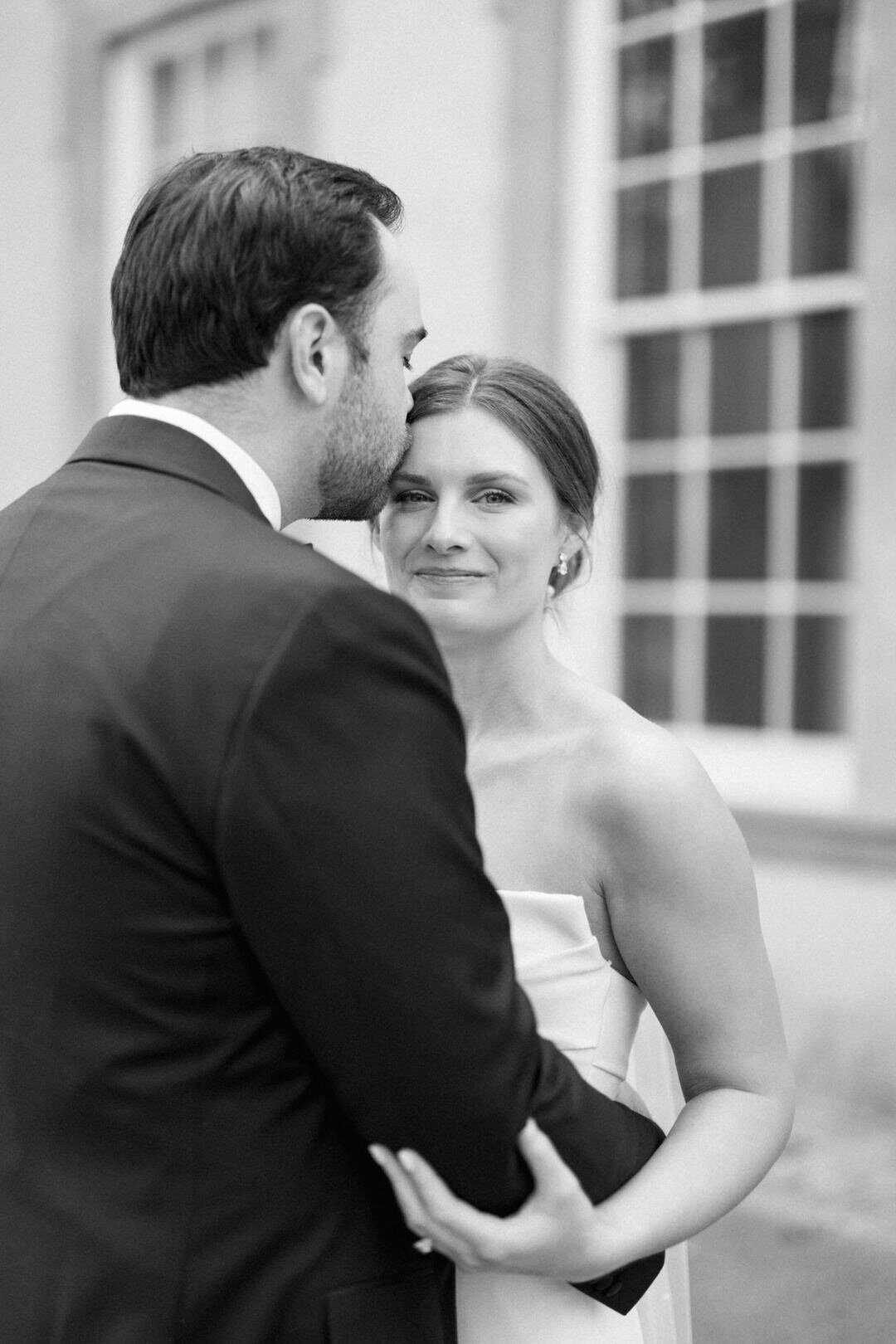 Black and White of Groom Kissing Bride on Head