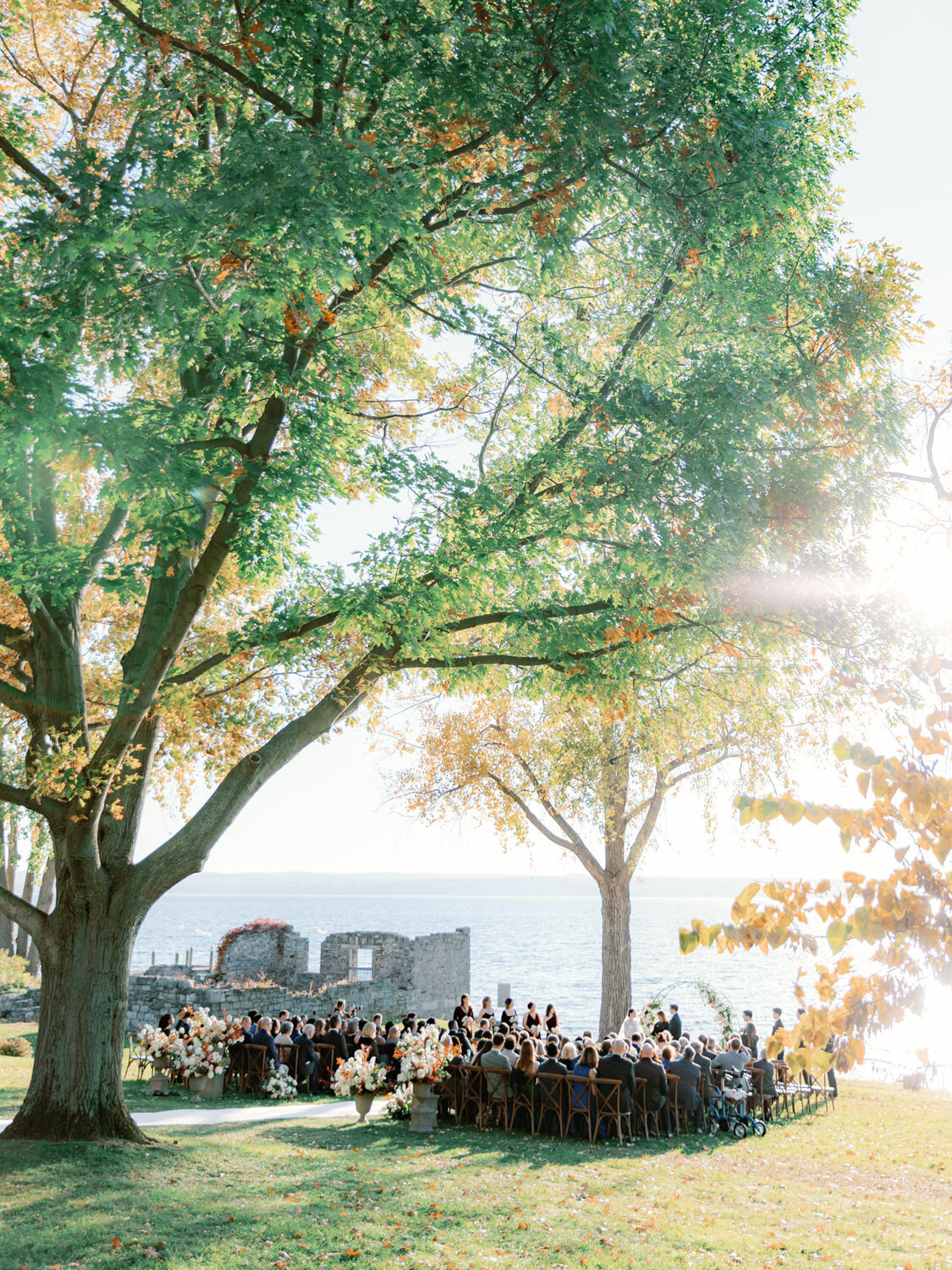 Wide photo of wedding ceremony on the lawn of Inns of Aurora with the Finger Lakes in the background.