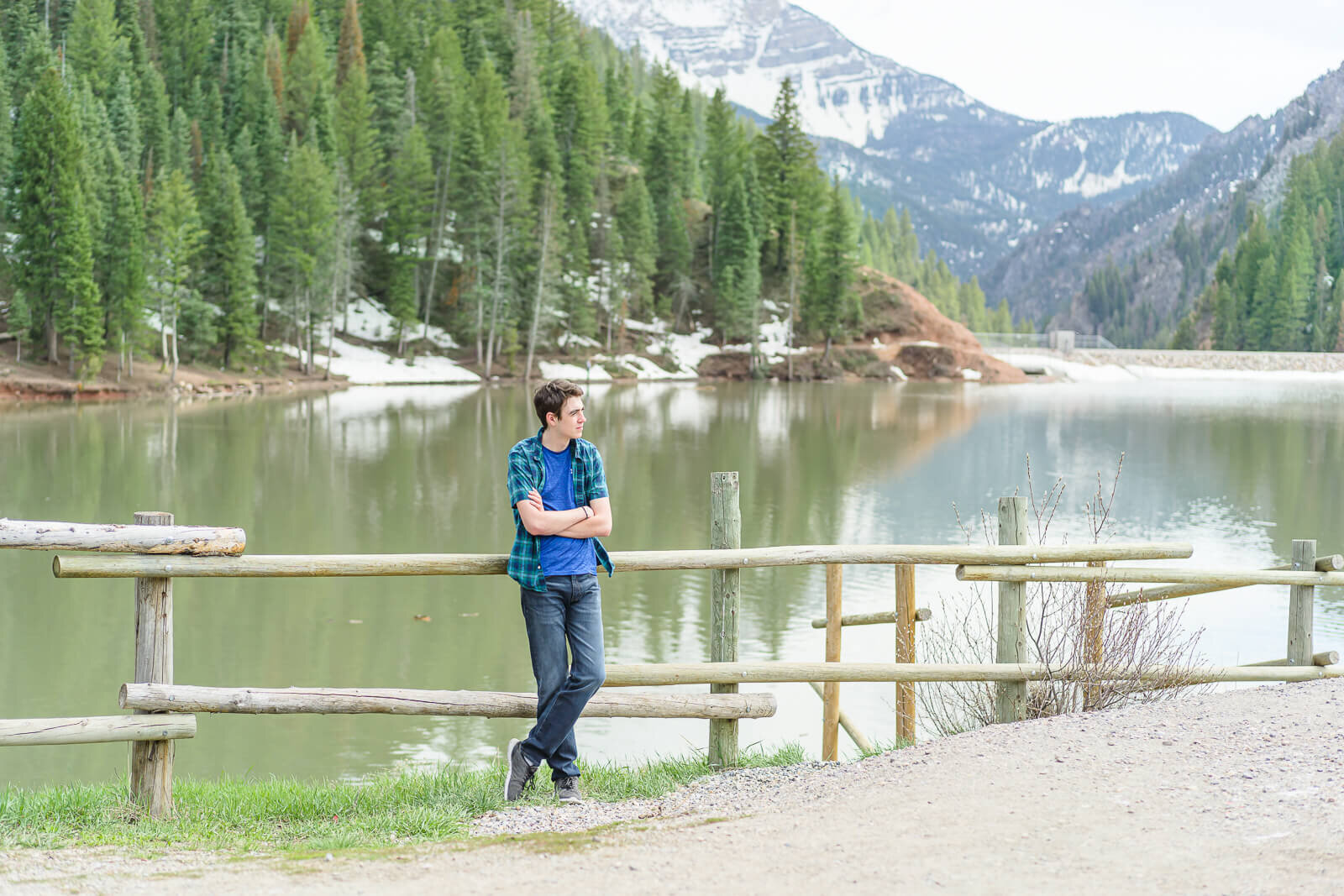 A high school senior boy stands in front of a fence by the shore of Tibble Fork reservoir in early spring. Captured by Salt Lake City senior photographer Melissa Woodruff Photography
