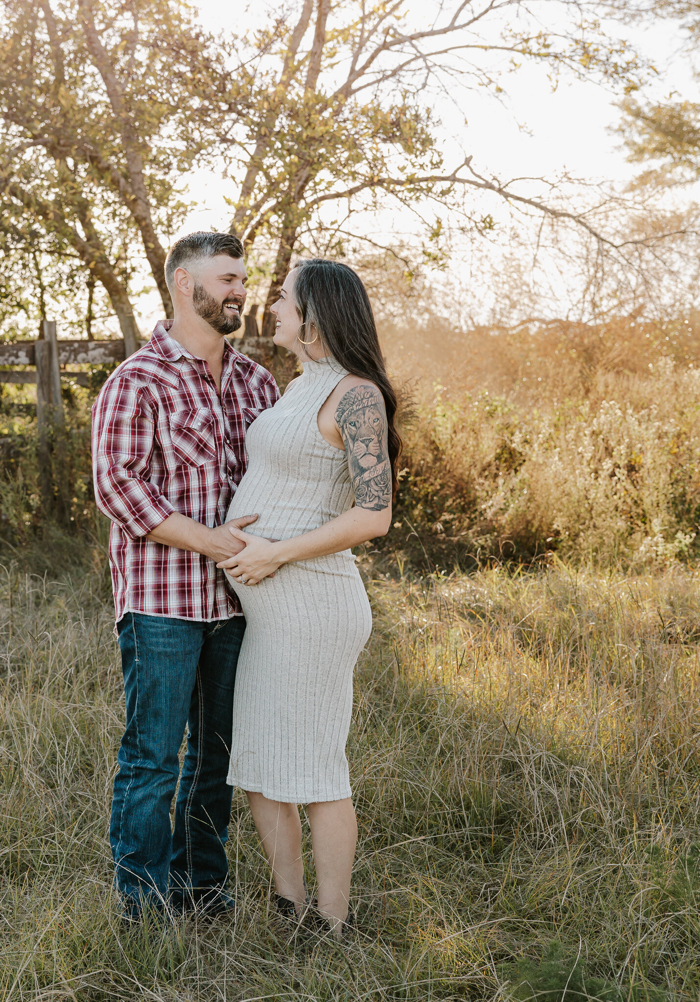 Outdoor maternity session in Aiken SC - expecting couple standing together in a golden field, holding her baby bump during sunset.