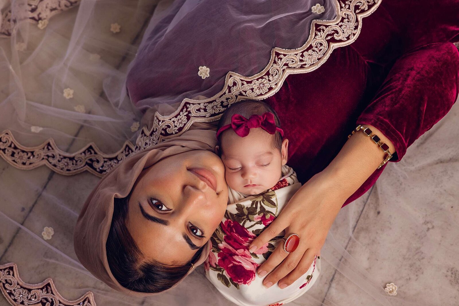 A woman in a veil tenderly holds a newborn baby during an in-home photography session by Bia Schaefer in Orlando.