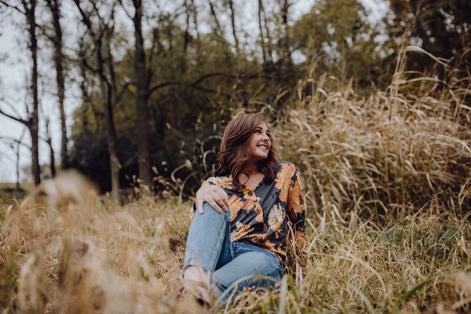 Girl sitting in field, hand on her knee. She's looking over her shoulder and smiling.