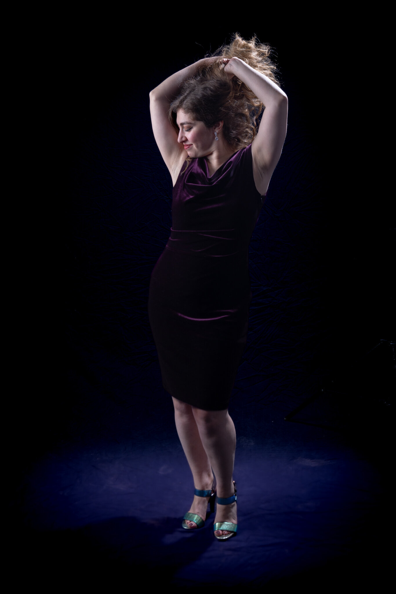 Nicole of Charizma Entertainment posing in velvet dress with hands above her head