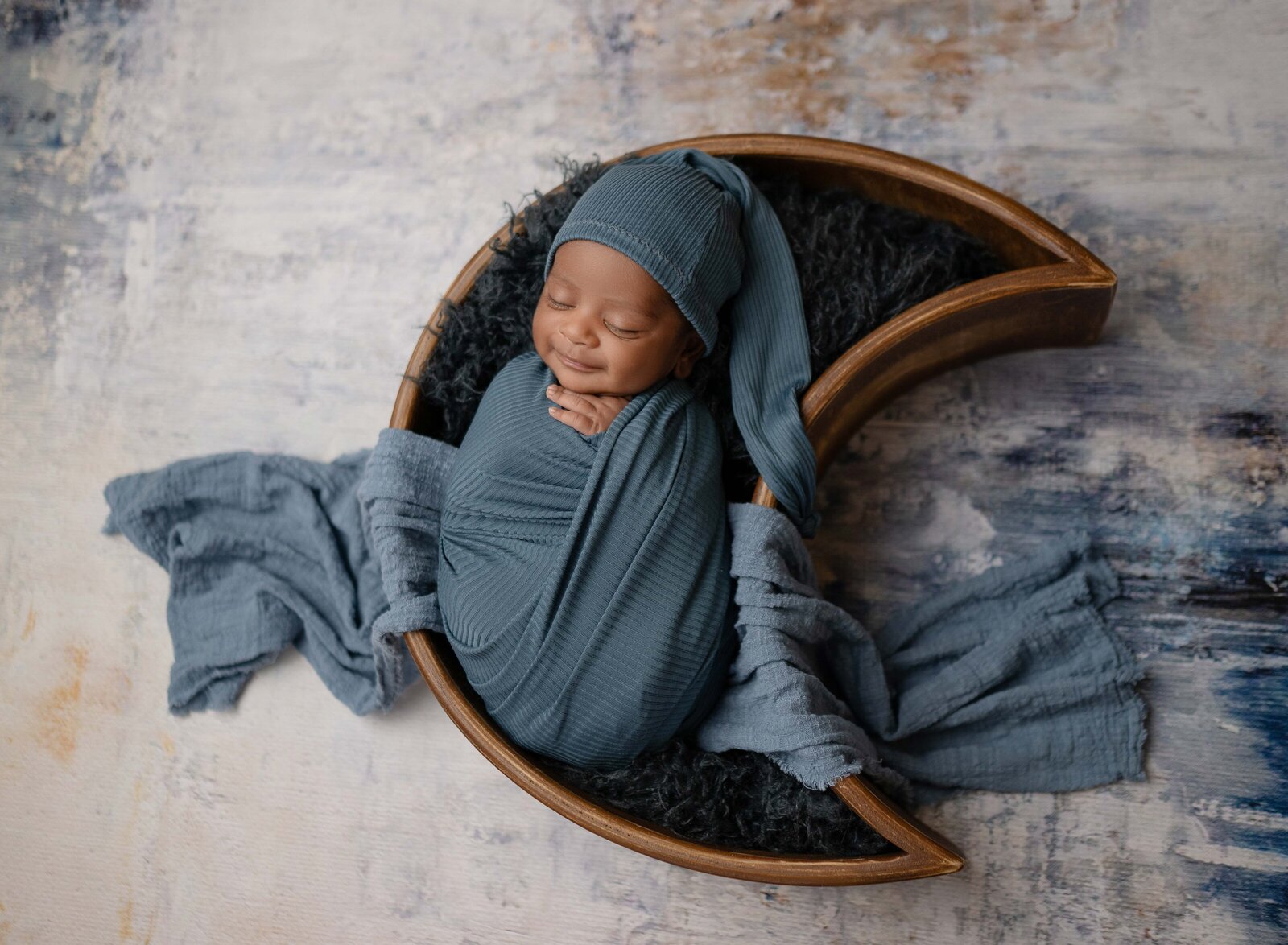 Baby sleeping in wooden moon bowl and swaddled in blue wrap. Newborn Photography session photographed at Jenni Nikki's photo studio in Marietta, GA, near Atlanta.