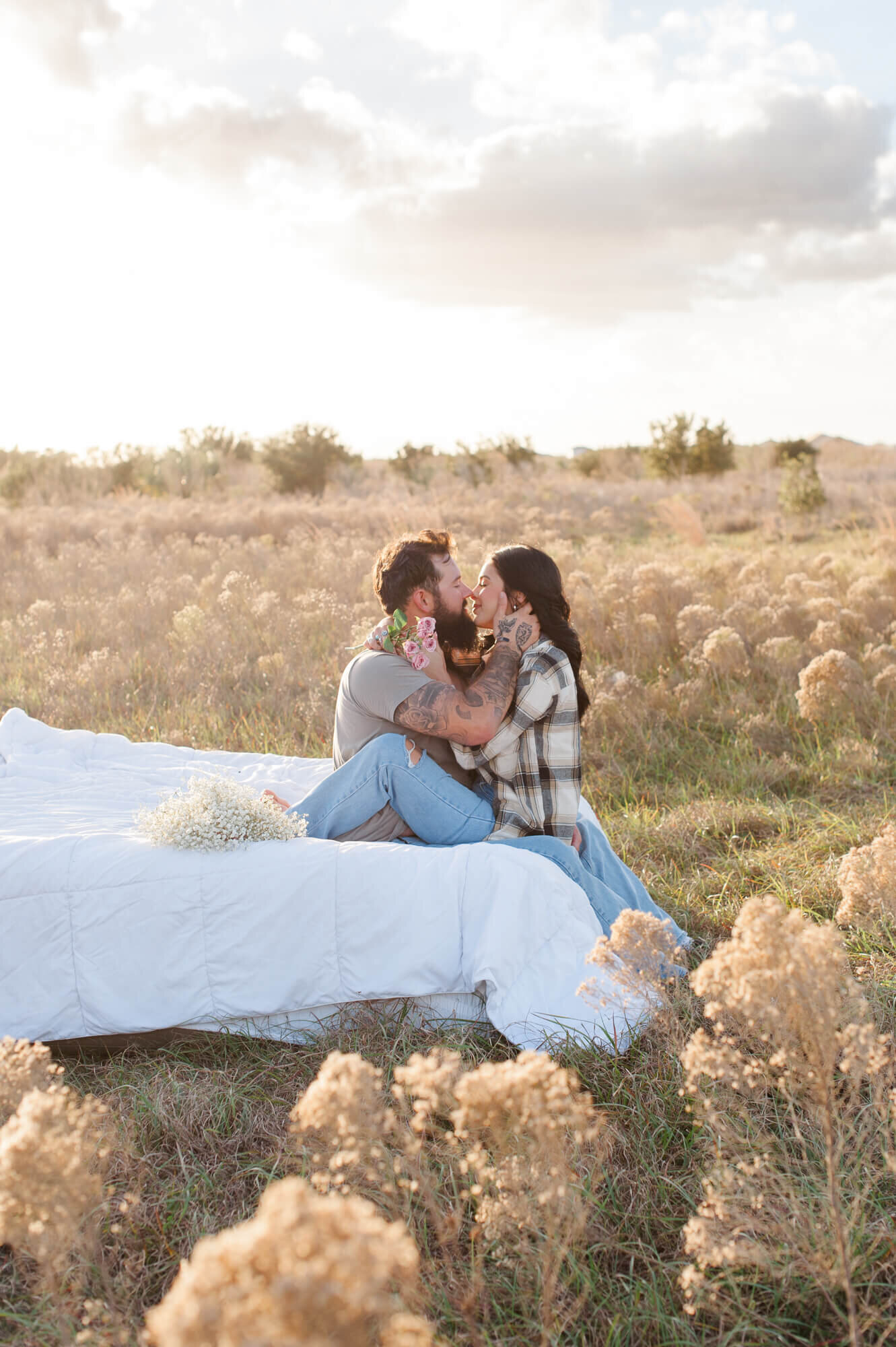 Couple kissing while holding each other on an air mattress in the middle of a tall grass field