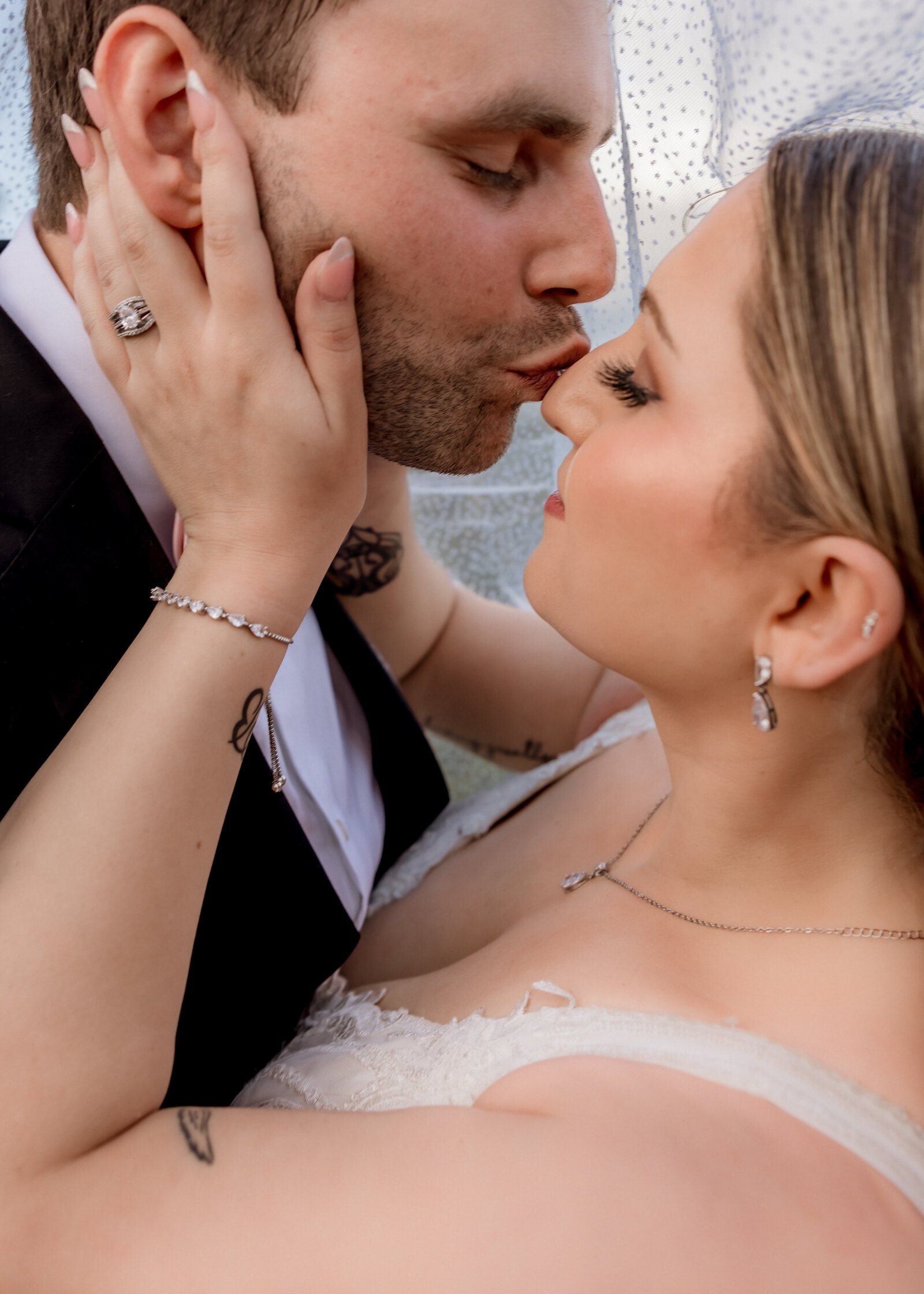 Groom kissing his bride on the nose under the veil.