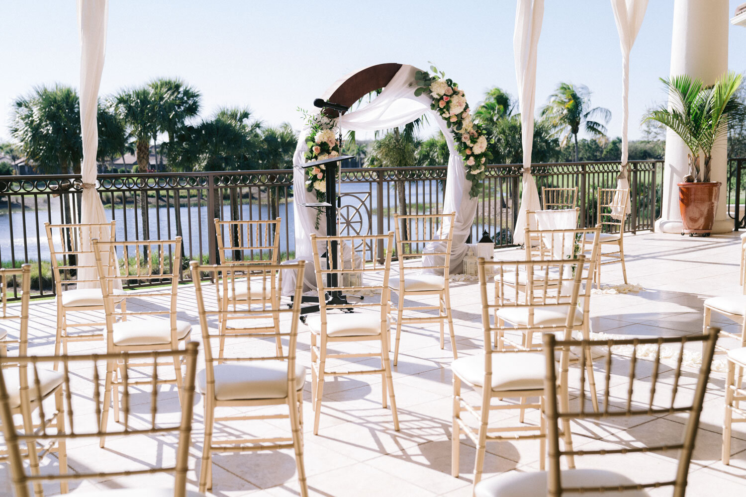 Ceremony setup with gold chairs and floral arch on a terrace with water views