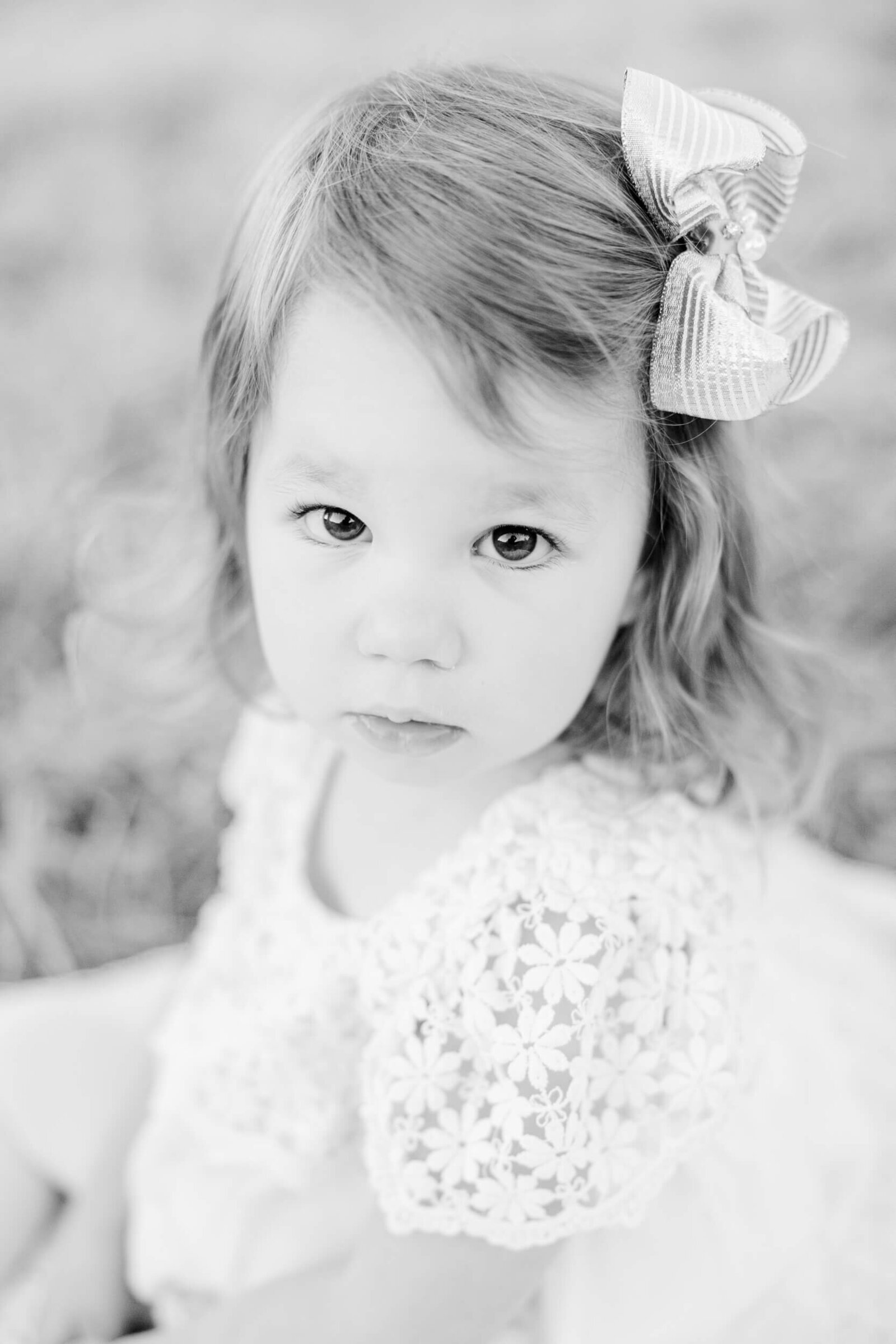 black and white, little girl in a white dress looks toward the viewer