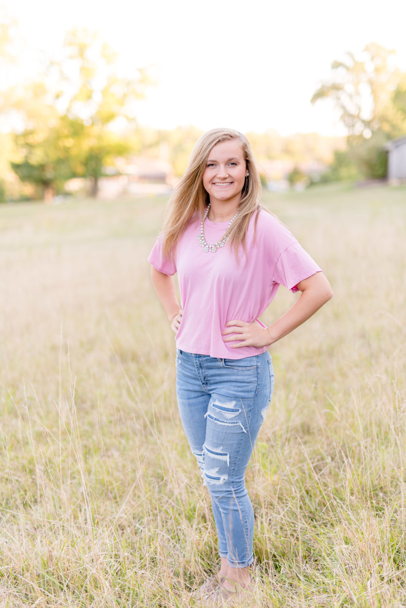 Senior stands in field and smiles.