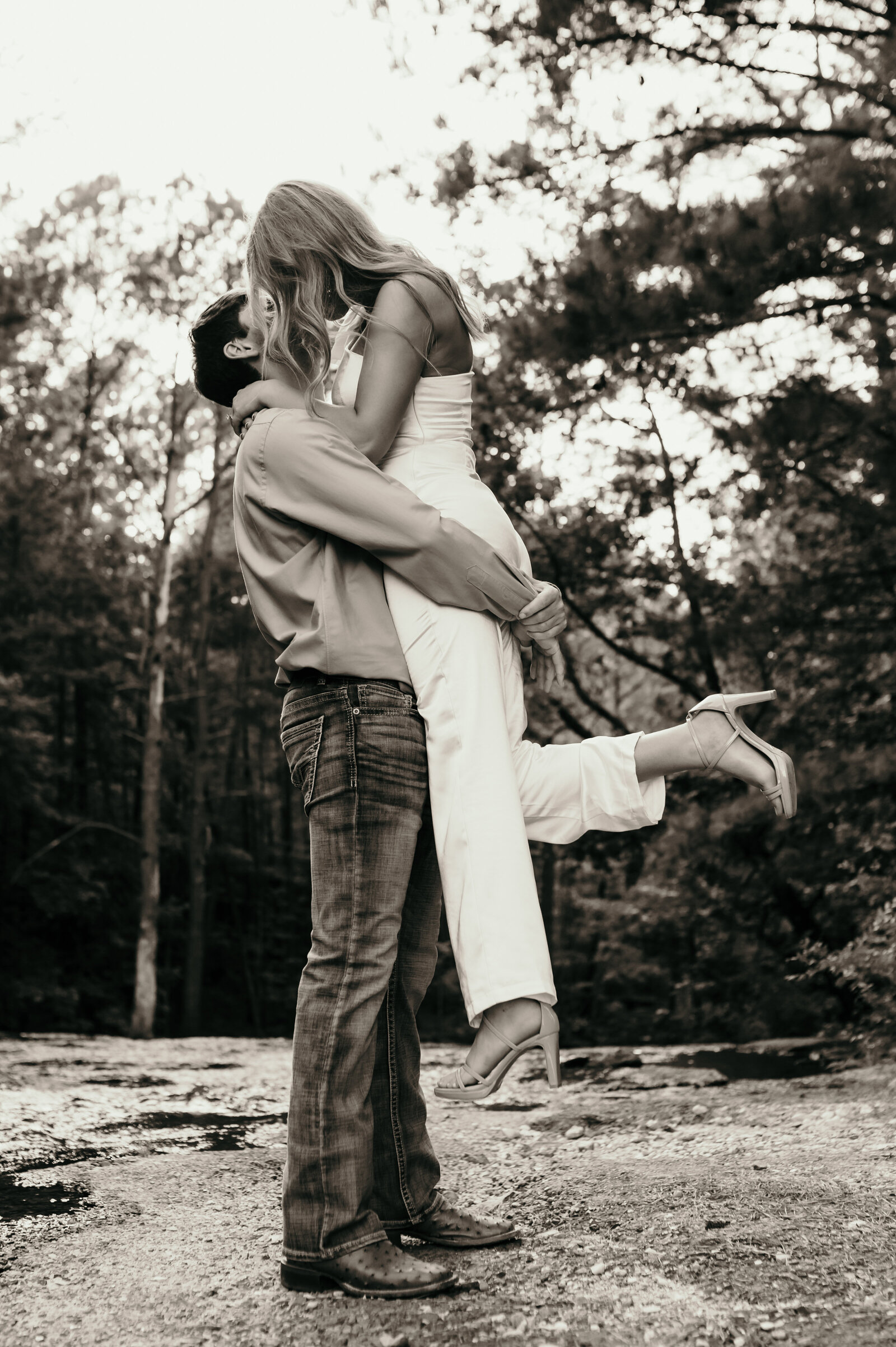 black and white outdoor engagement photos in little rock ar with man picking up his fiance as they kiss each other